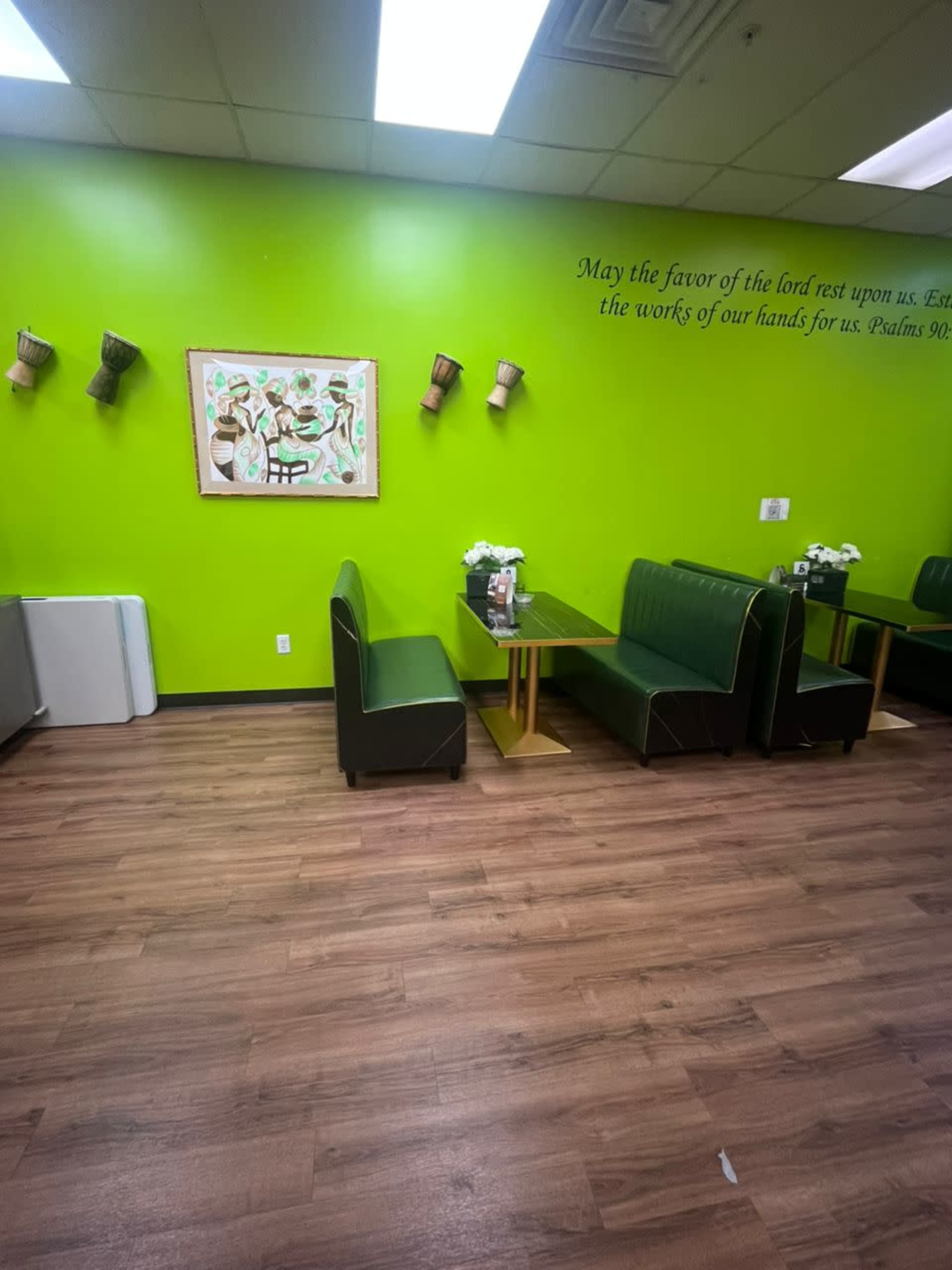 The image shows a vibrant green restaurant interior with wooden flooring, featuring two green booths and a wall decoration with artwork and text.