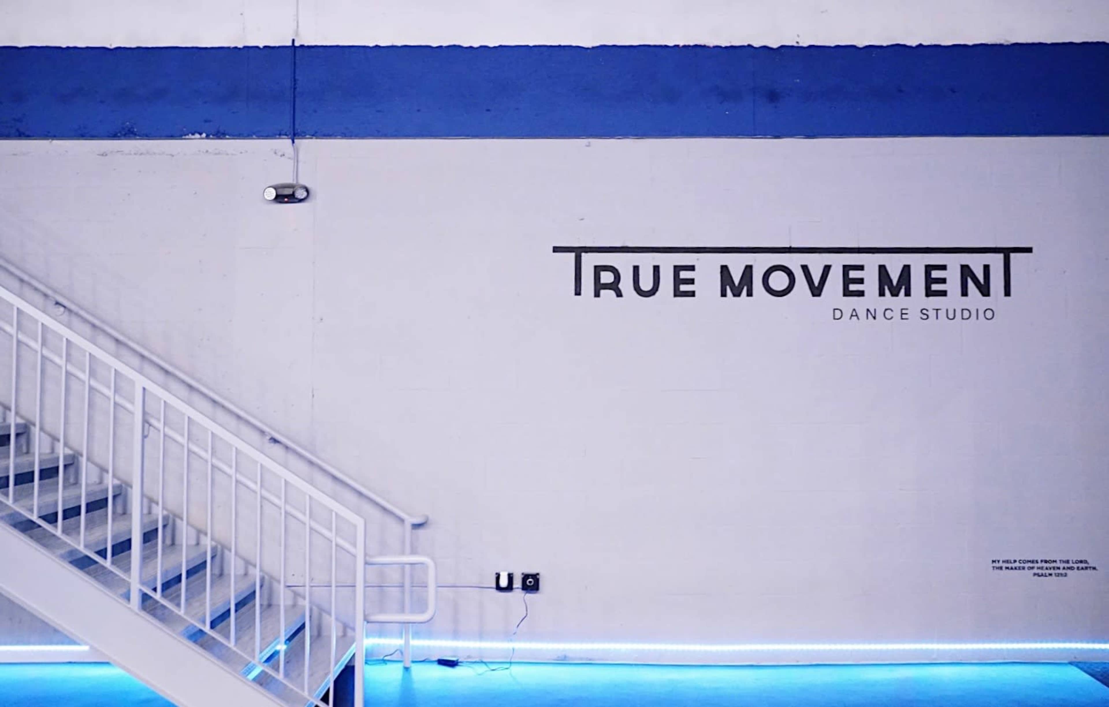 The image shows a staircase next to a blue and white wall featuring the text "TRUE MOVEMENT DANCE STUDIO."