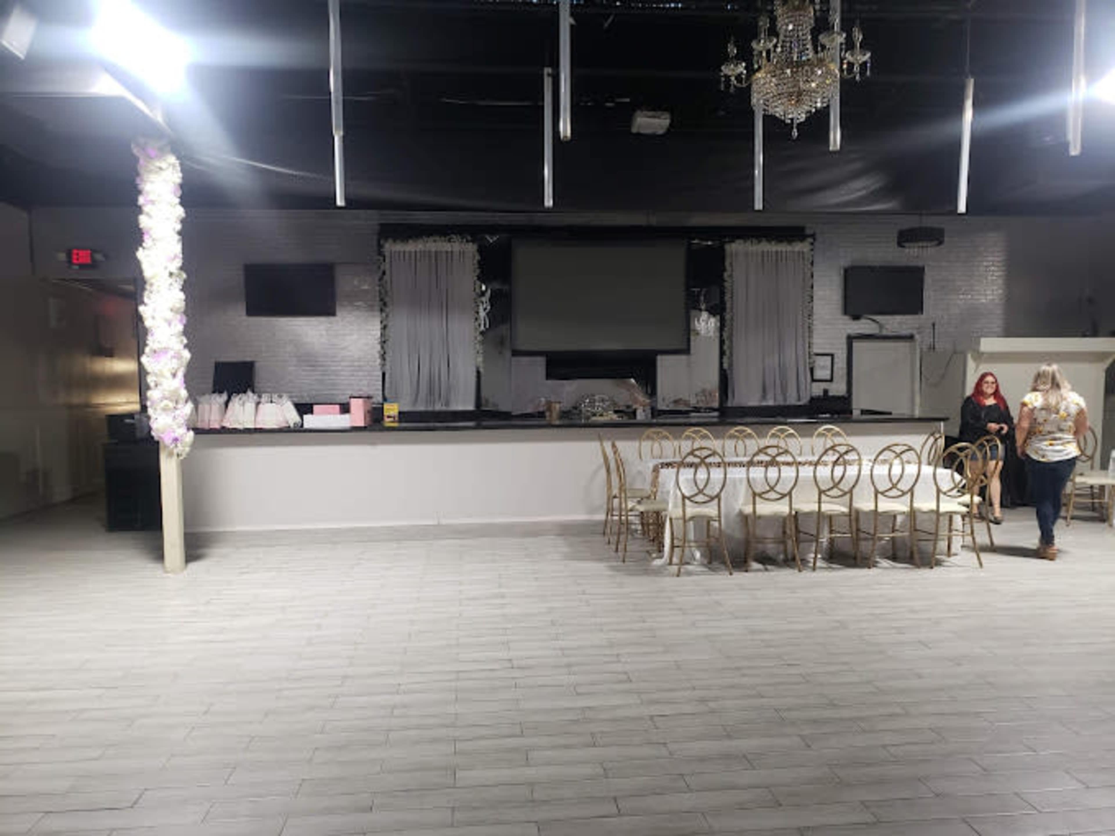 A spacious event venue with a large, empty seating area and a stage at the front, adorned with chandeliers and decorative drapes.