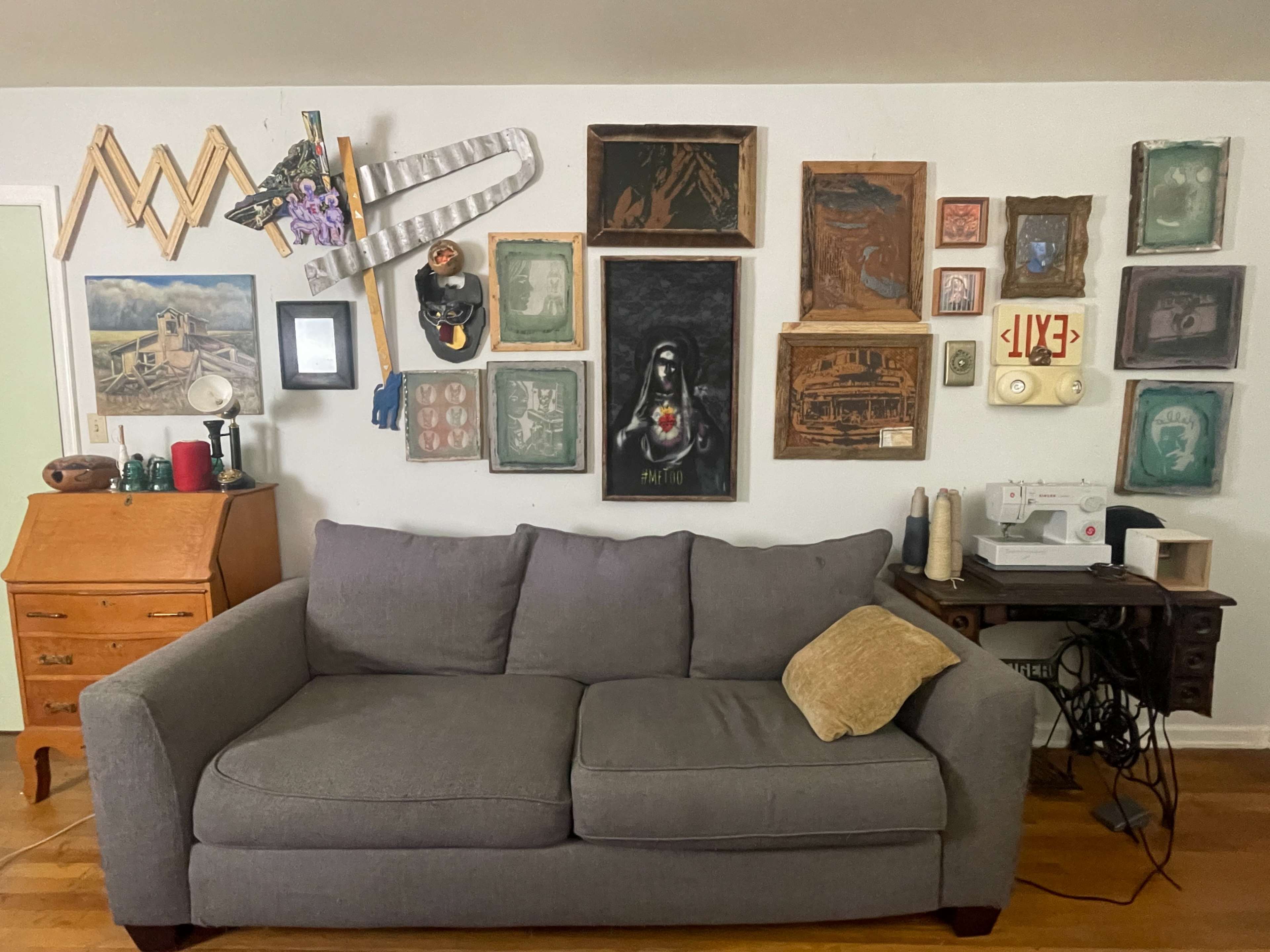 A gray sofa is positioned in front of a gallery wall featuring various framed artworks and decorative items.