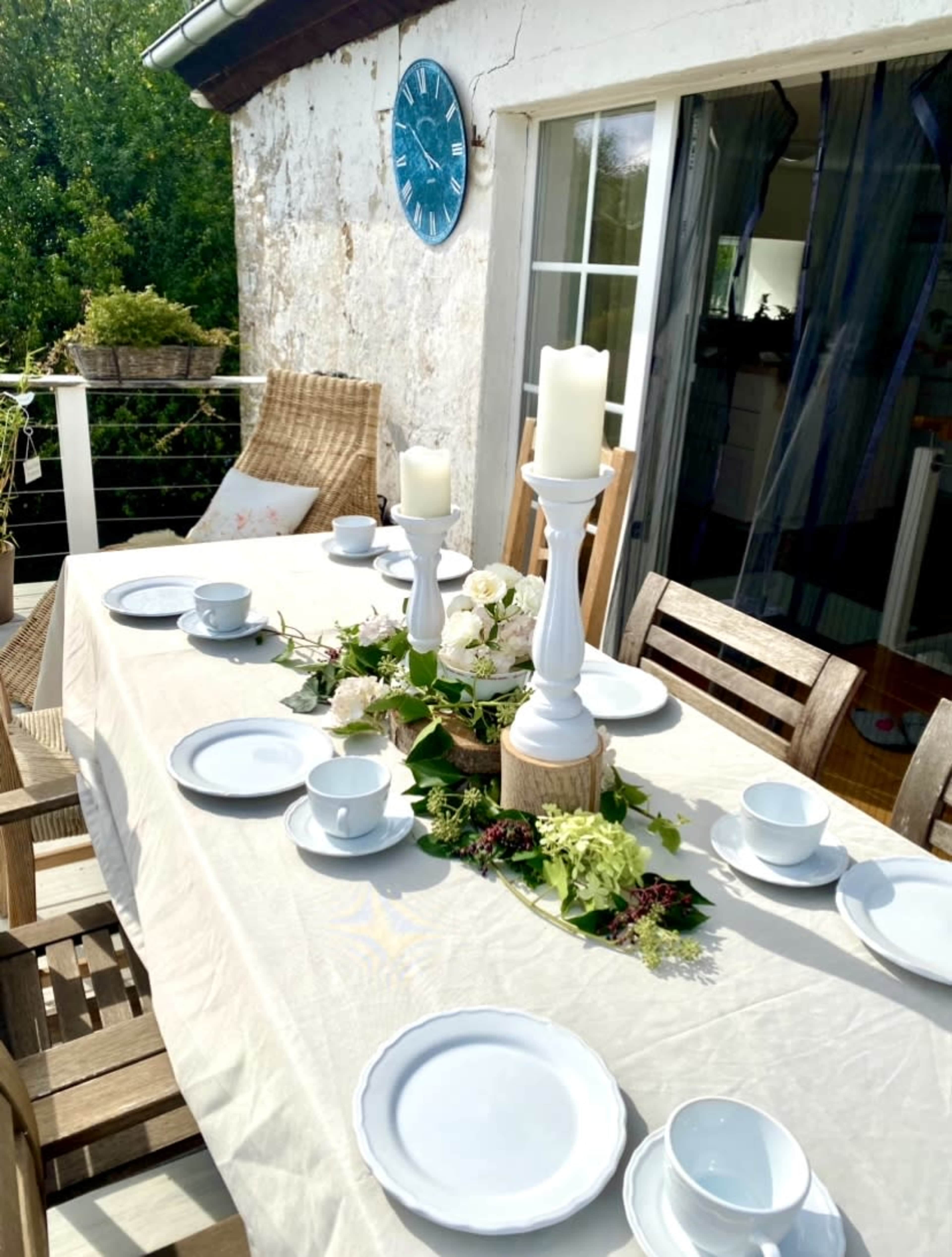 A table is set on a patio with white dishes, decorative candles, and green foliage, overlooking a natural landscape.