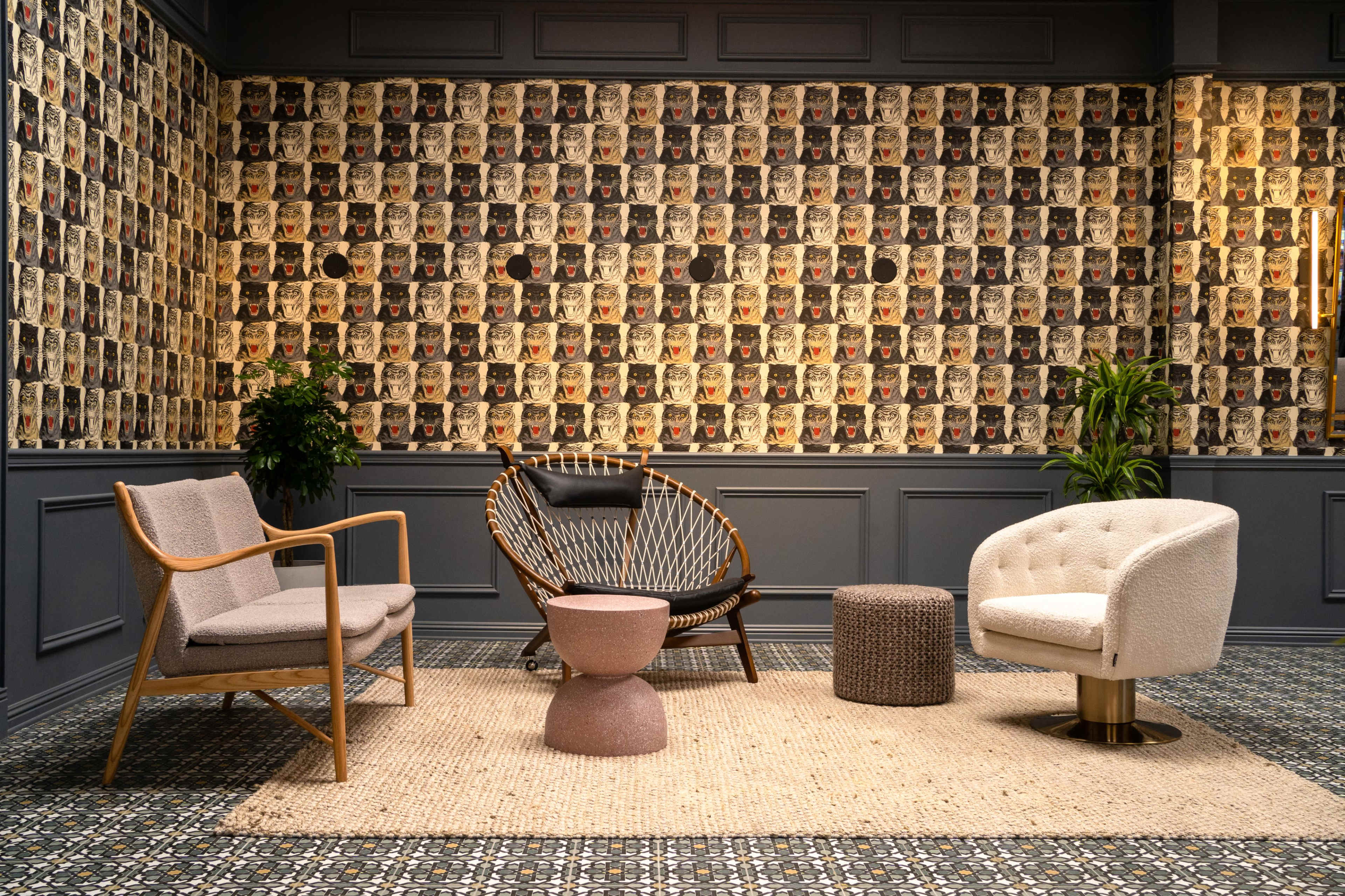 A modern sitting area features three chairs and a central table on a patterned rug, surrounded by a wall adorned with vintage-style portraits.