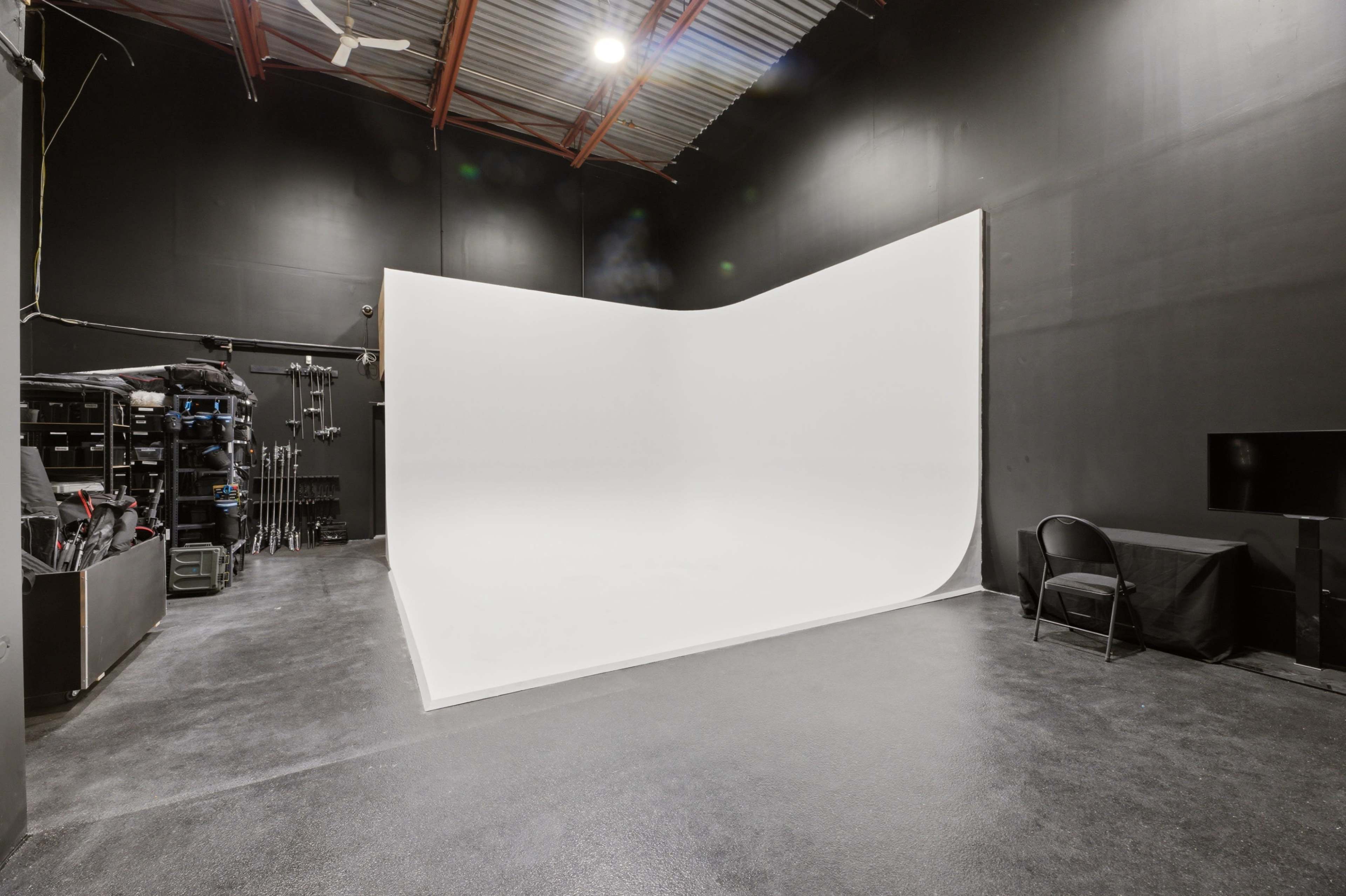 The image depicts a photography studio featuring a large, seamless white backdrop against a black wall and floor.