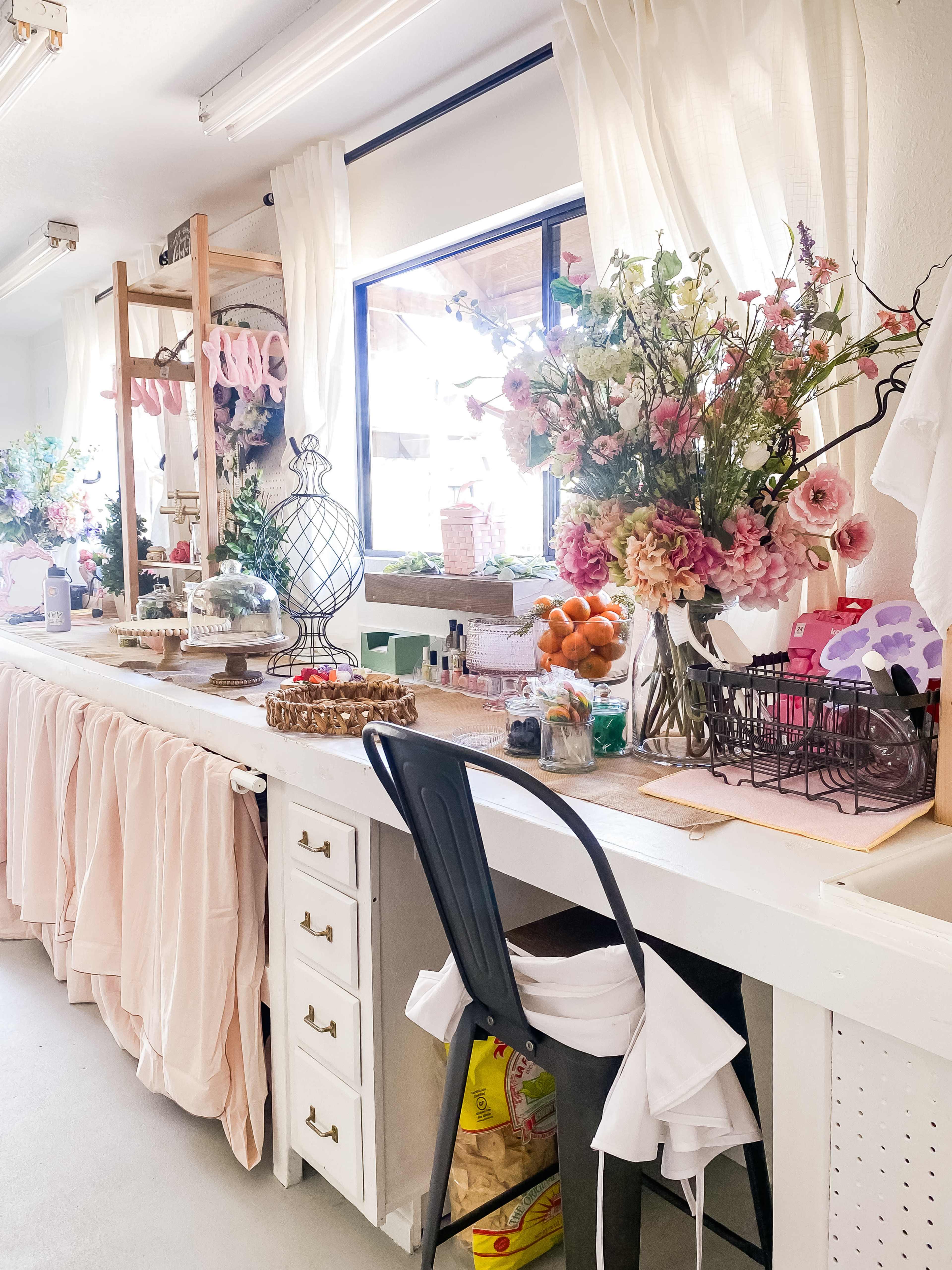 A bright room features a white table adorned with flowers, decorative items, and fruit, next to a black chair.