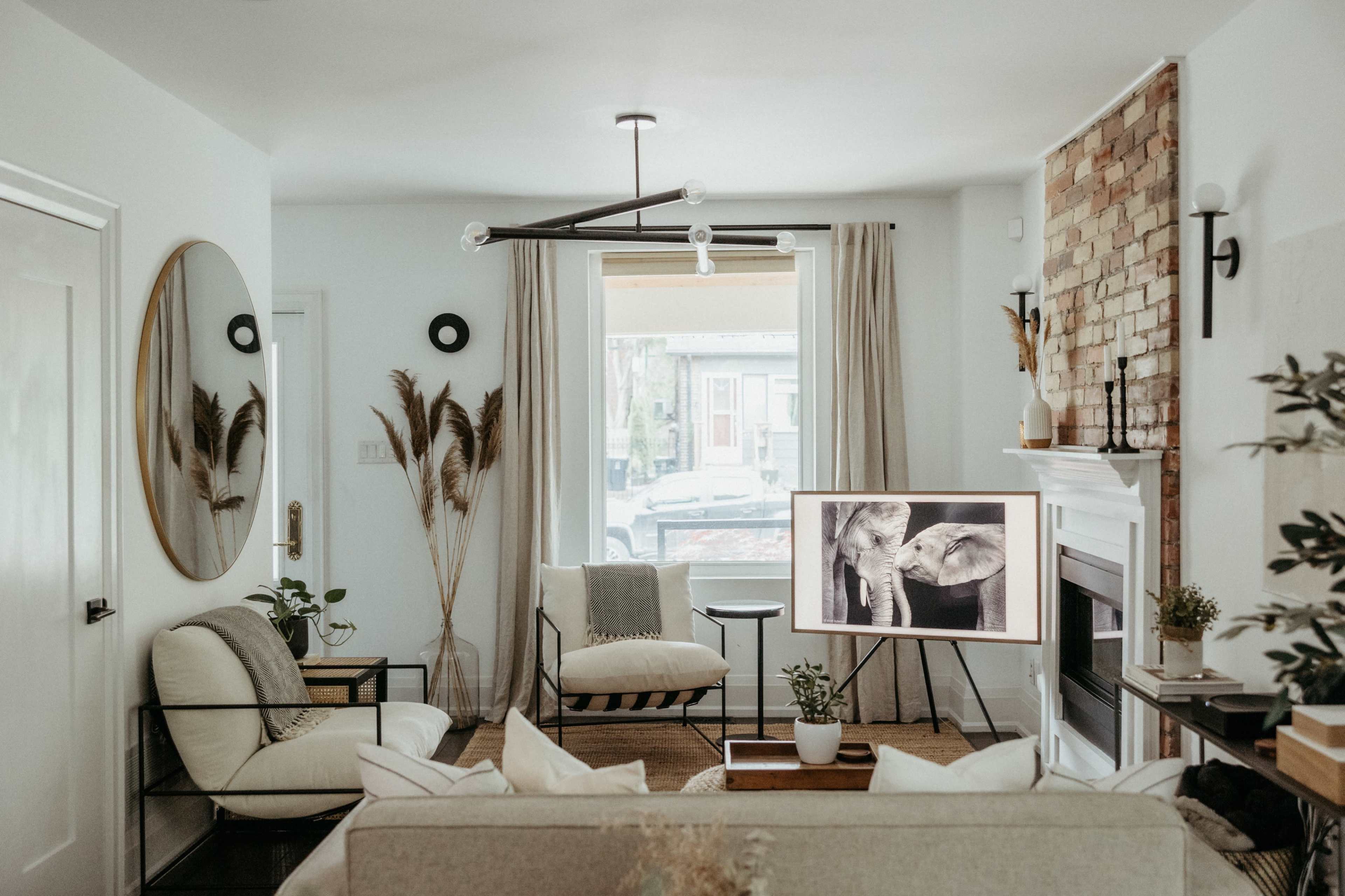 A living room with a neutral color palette, featuring comfortable seating, a large mirror, and a framed artwork of elephants on a stand.