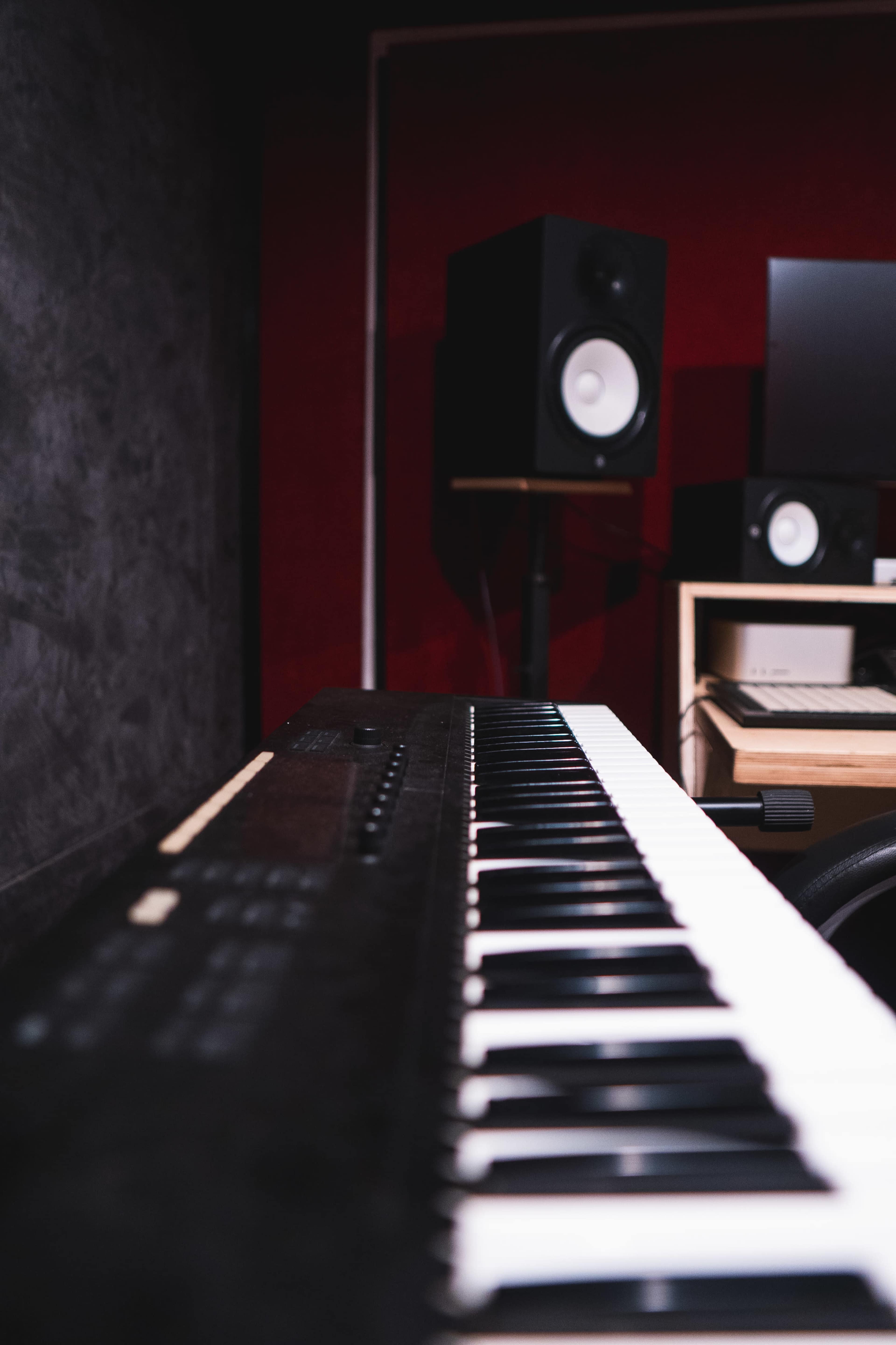 A close-up of a keyboard with piano keys in the foreground, with studio monitors and a computer setup in the background.