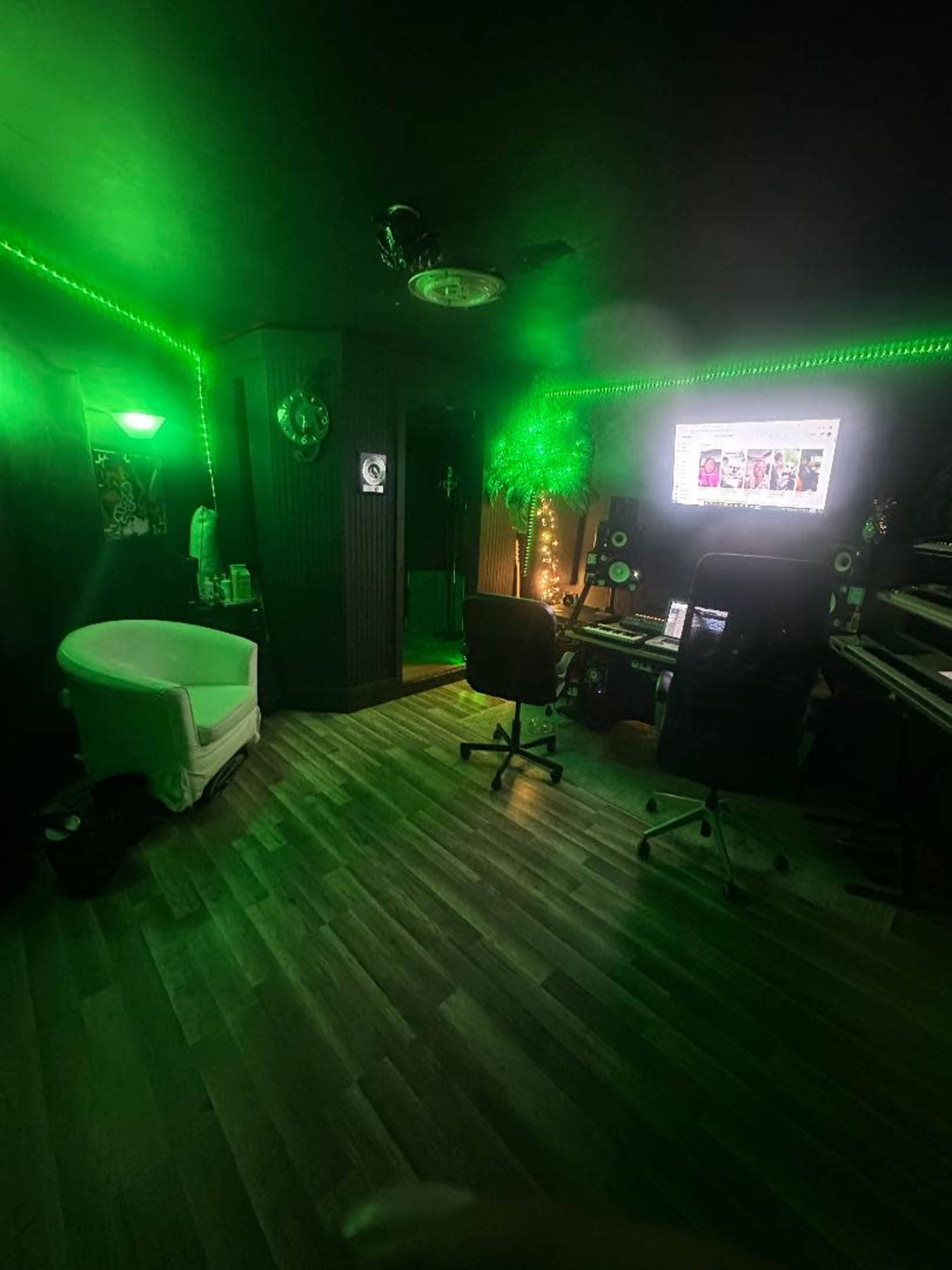 The image shows a music studio with green LED lights, a computer setup, and various musical instruments arranged in a dimly lit room.