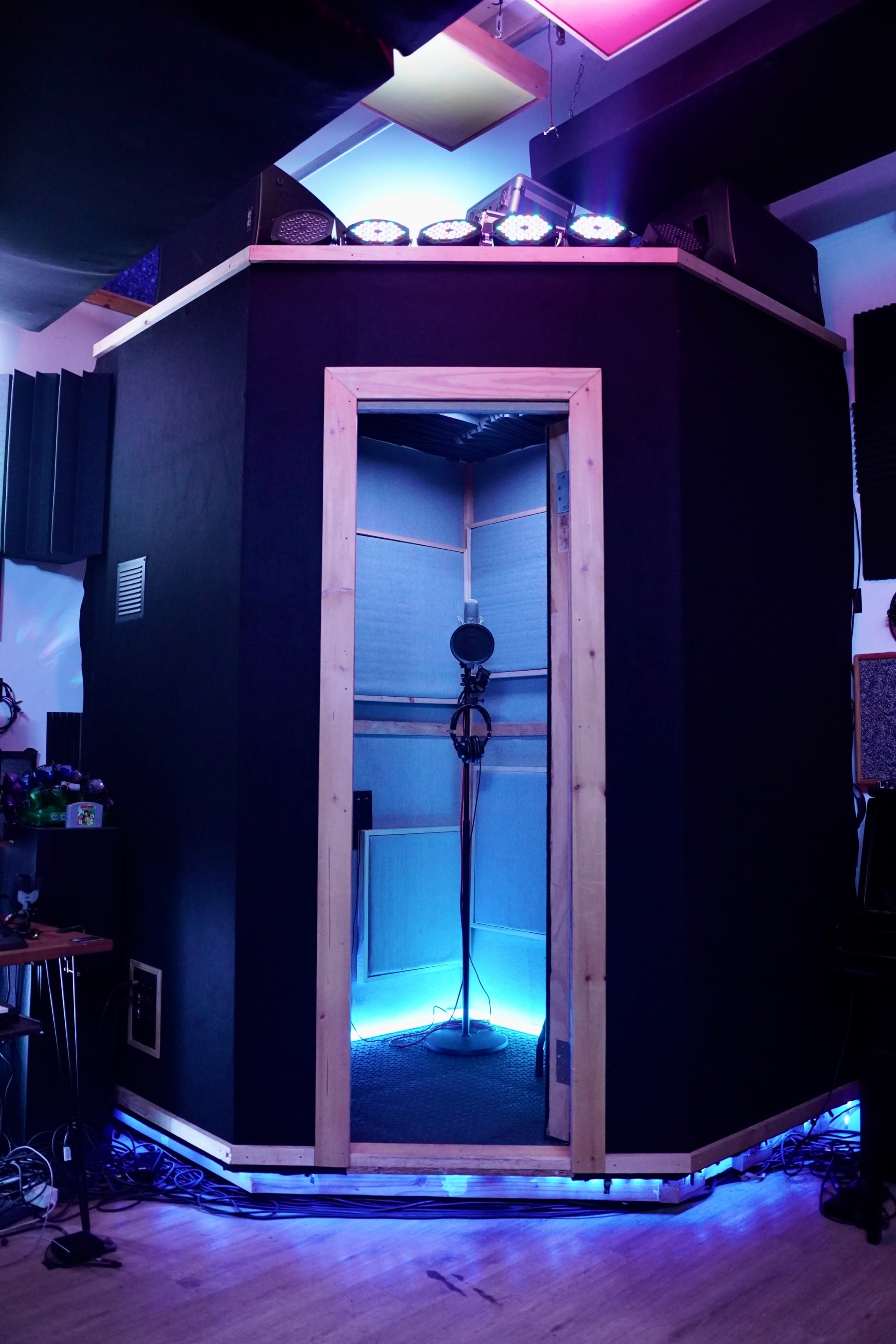 The image shows a soundproof vocal booth with soft blue lighting and a microphone stand inside.