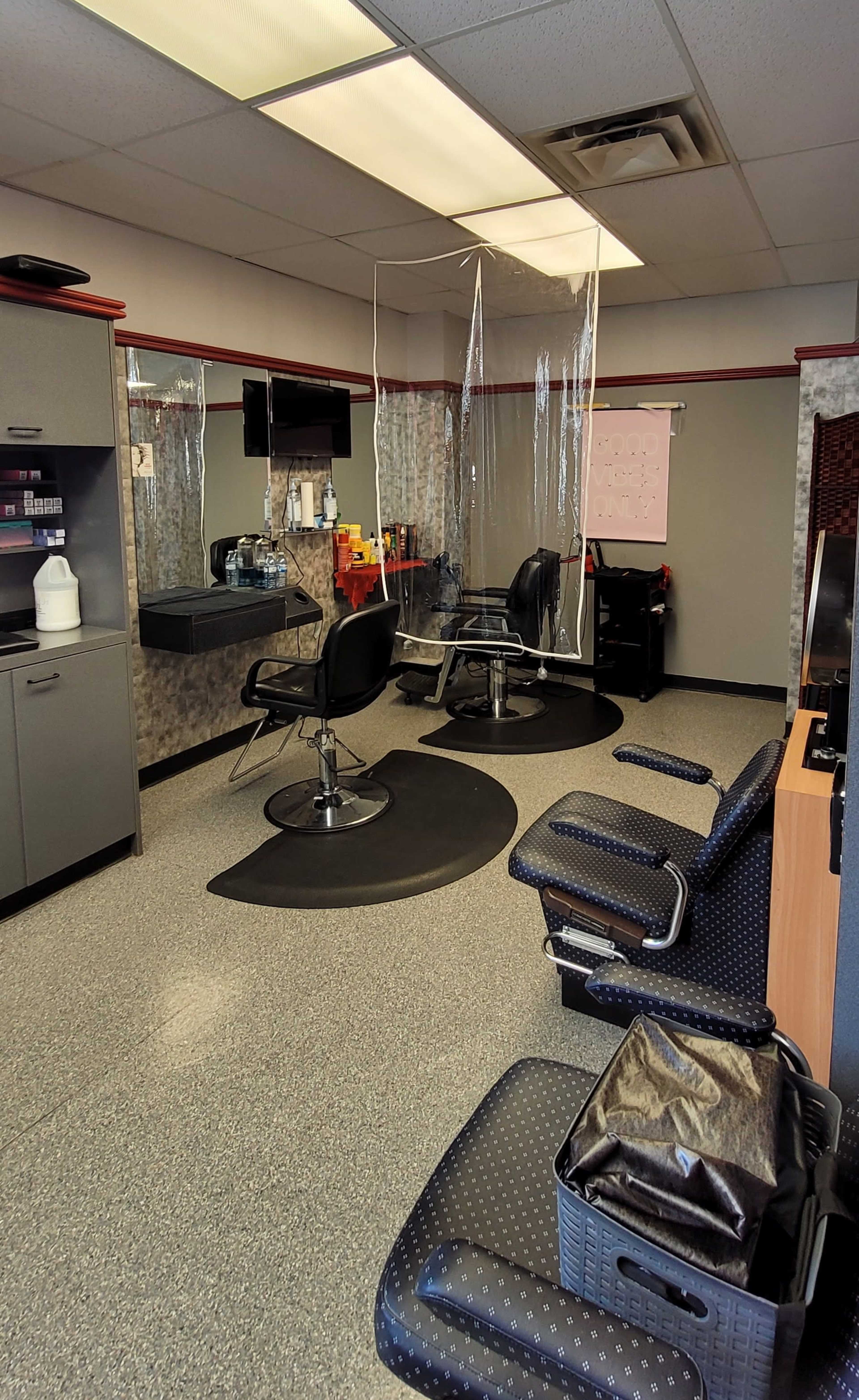 A barbershop interior with two barber chairs, a wall-mounted mirror, and a partition hanging from the ceiling.
