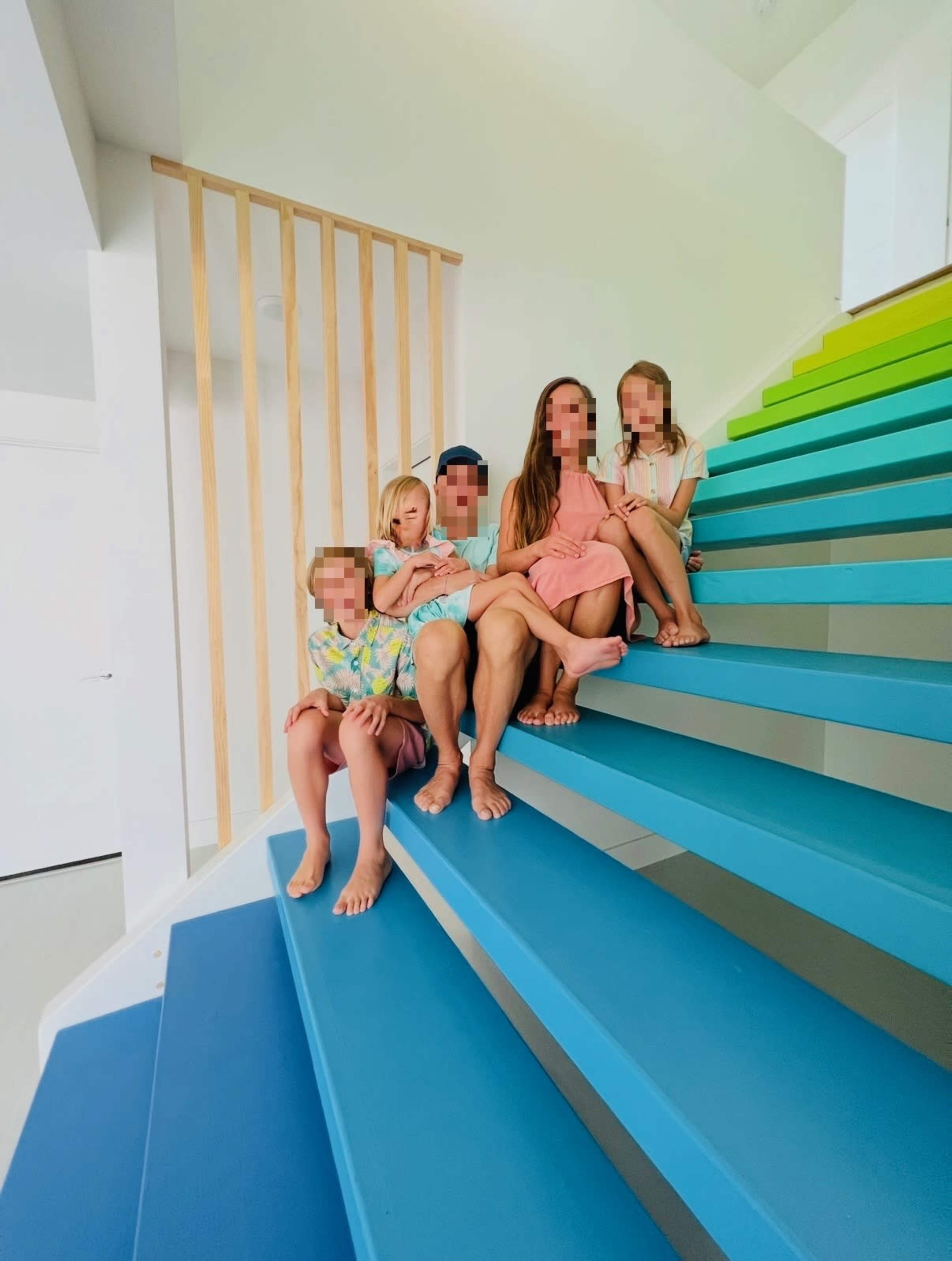 A family of five is sitting on a colorful staircase with blue and green steps.