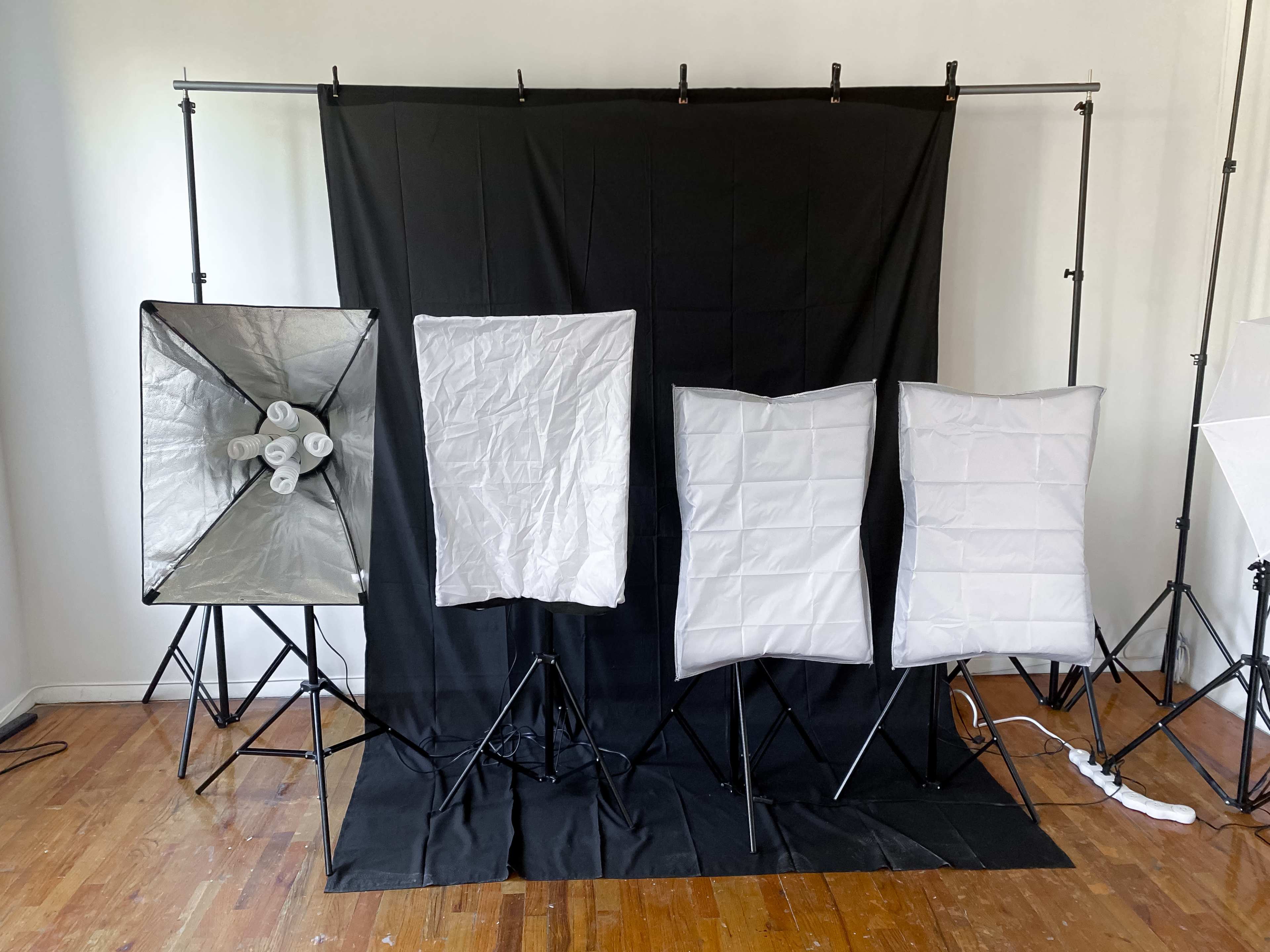 A photography setup with a black backdrop and several softboxes arranged in front of it.