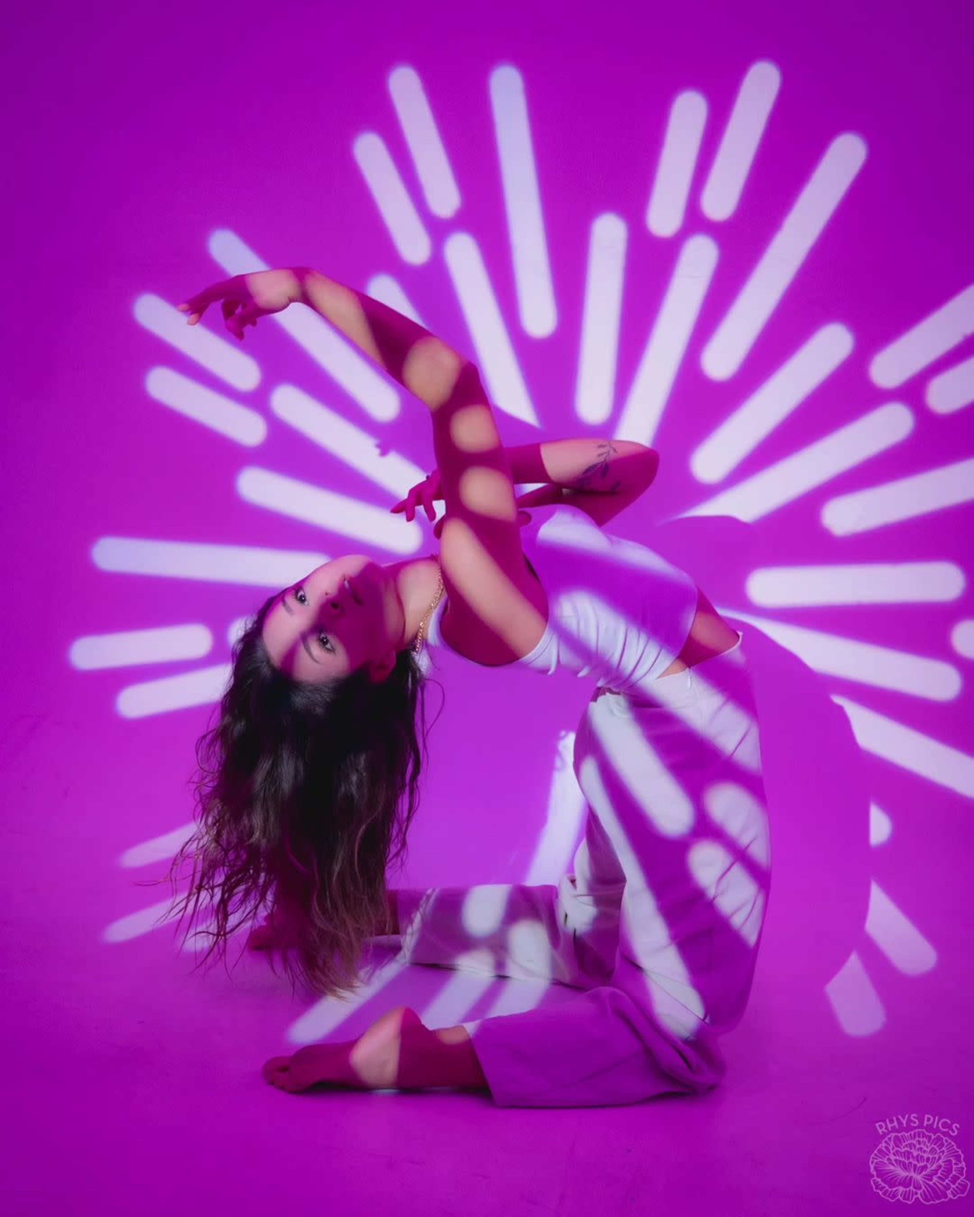 A dancer is posing on the floor, with her body contorted and illuminated by purple light casting dynamic shadows.