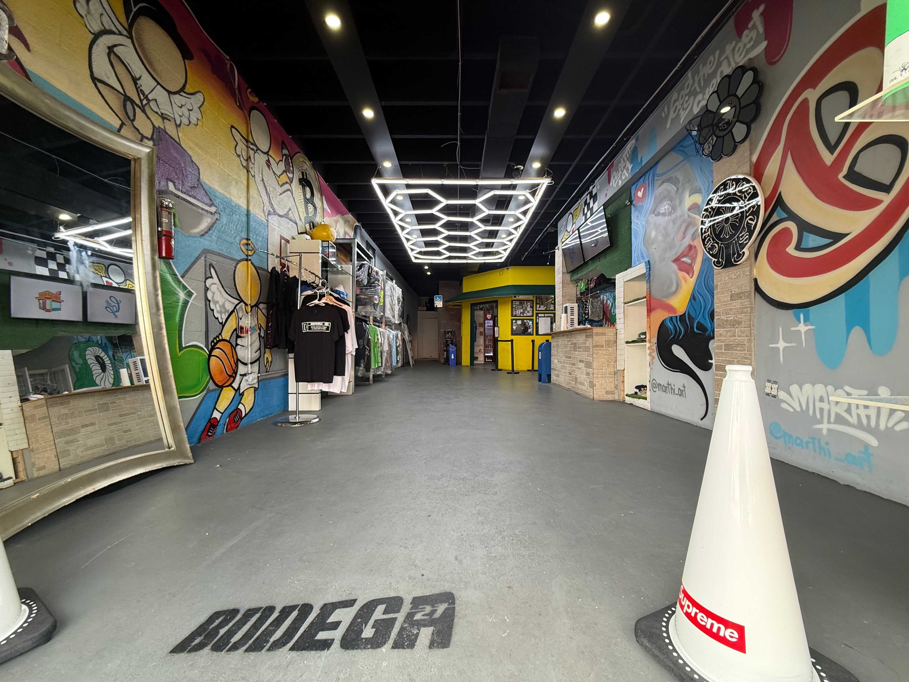 The image shows a modern store interior featuring graffiti-style murals on the walls, illuminated by central lighting and displaying merchandise such as clothing and accessories.