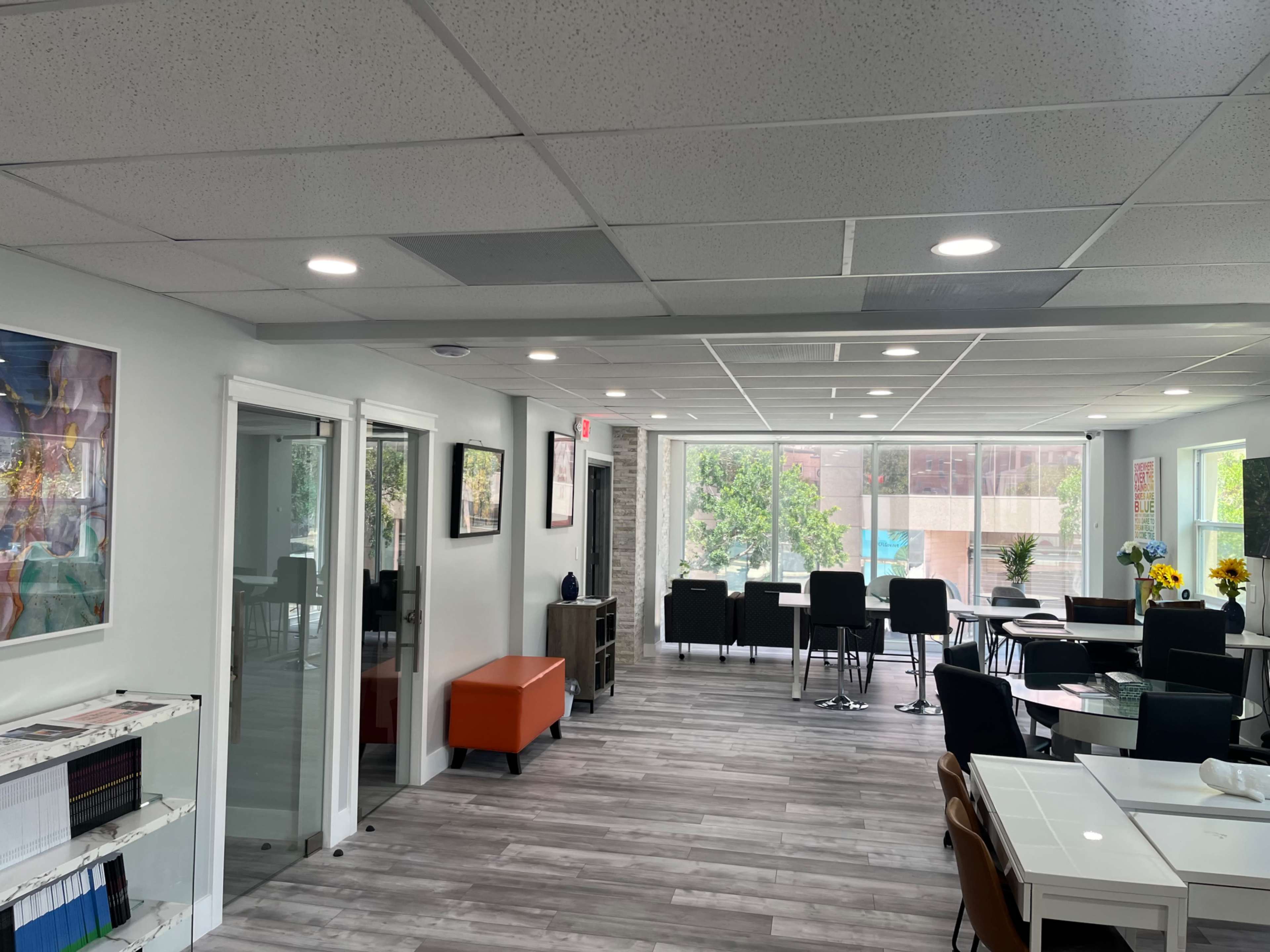 A modern office space with a reception area, tables, chairs, and large windows allowing natural light to enter.