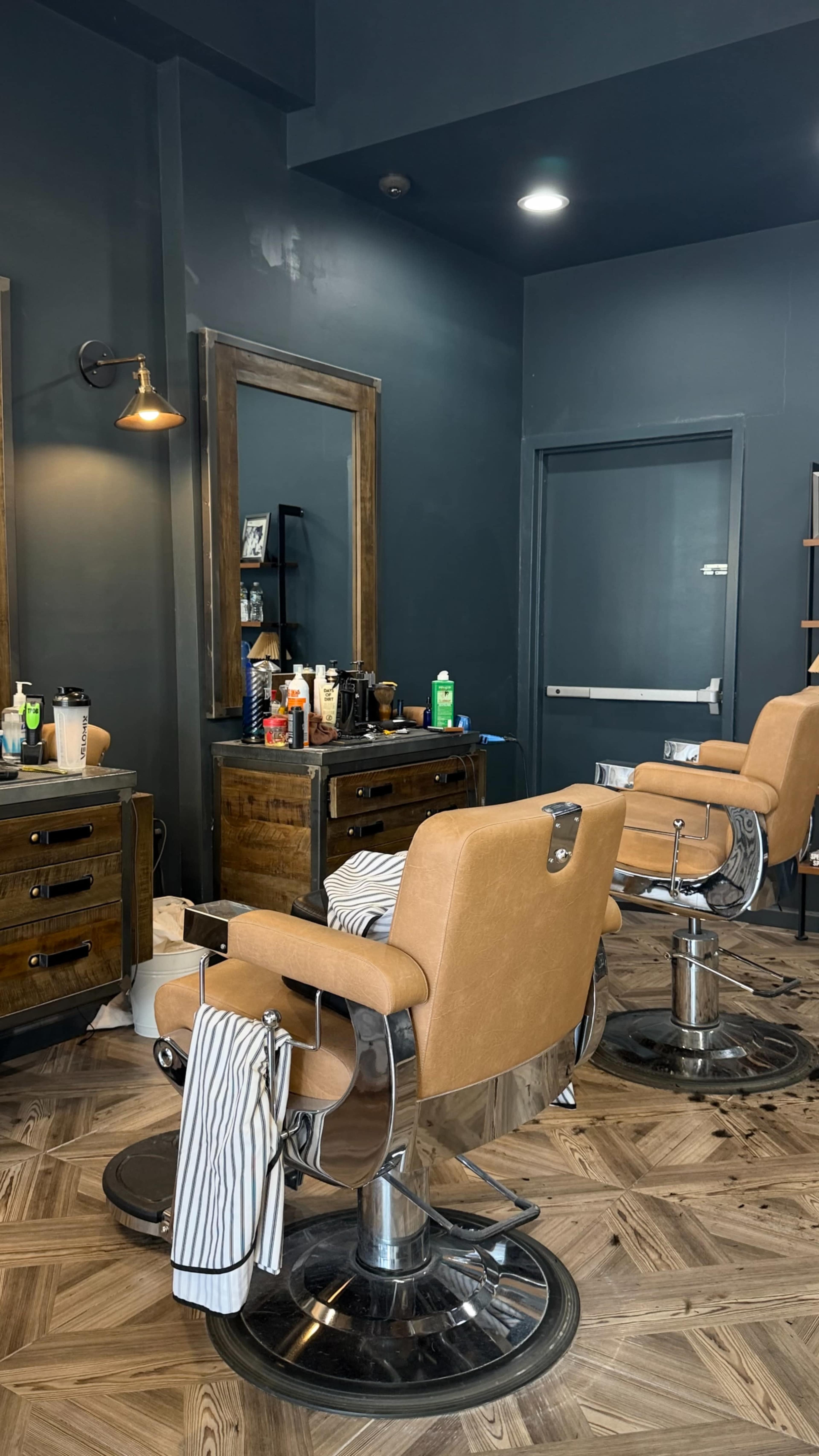 The image shows an interior of a hair salon with two barber chairs facing mirrors, surrounded by shelves and various hair products on display.