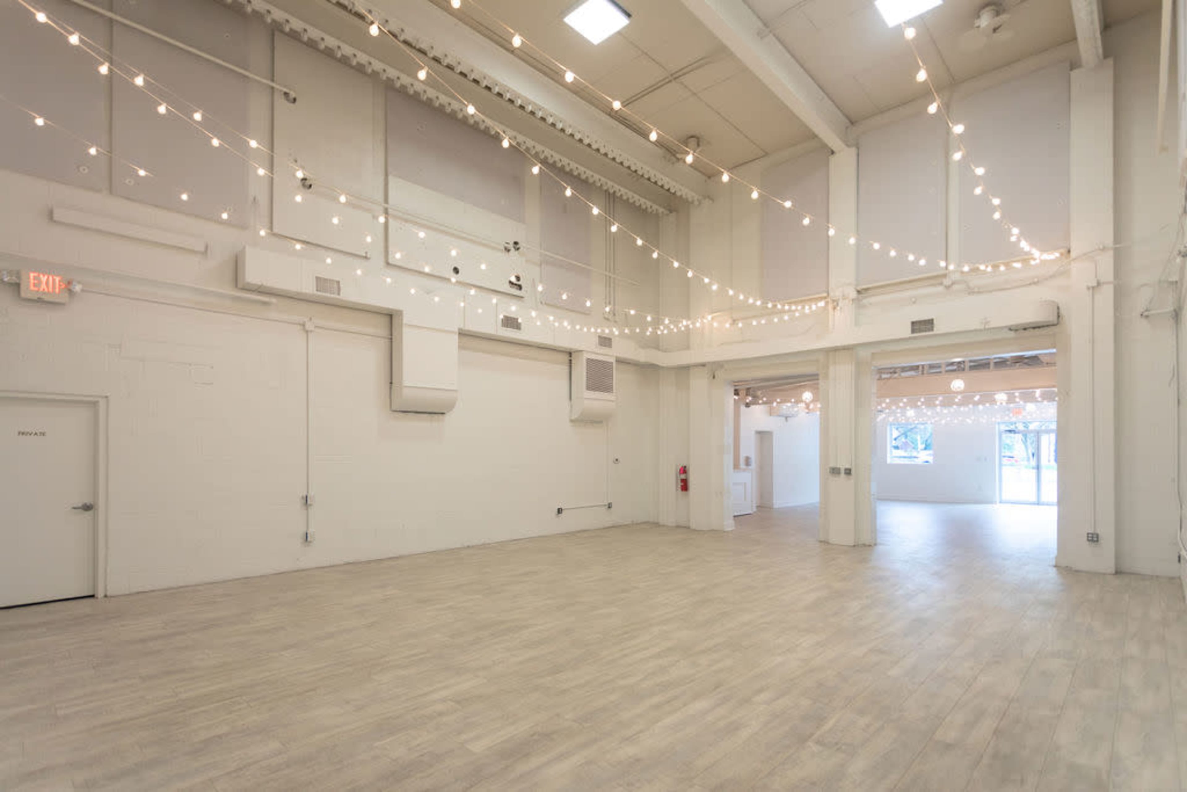 A large, open room with white walls, hardwood flooring, and string lights hanging from the ceiling.