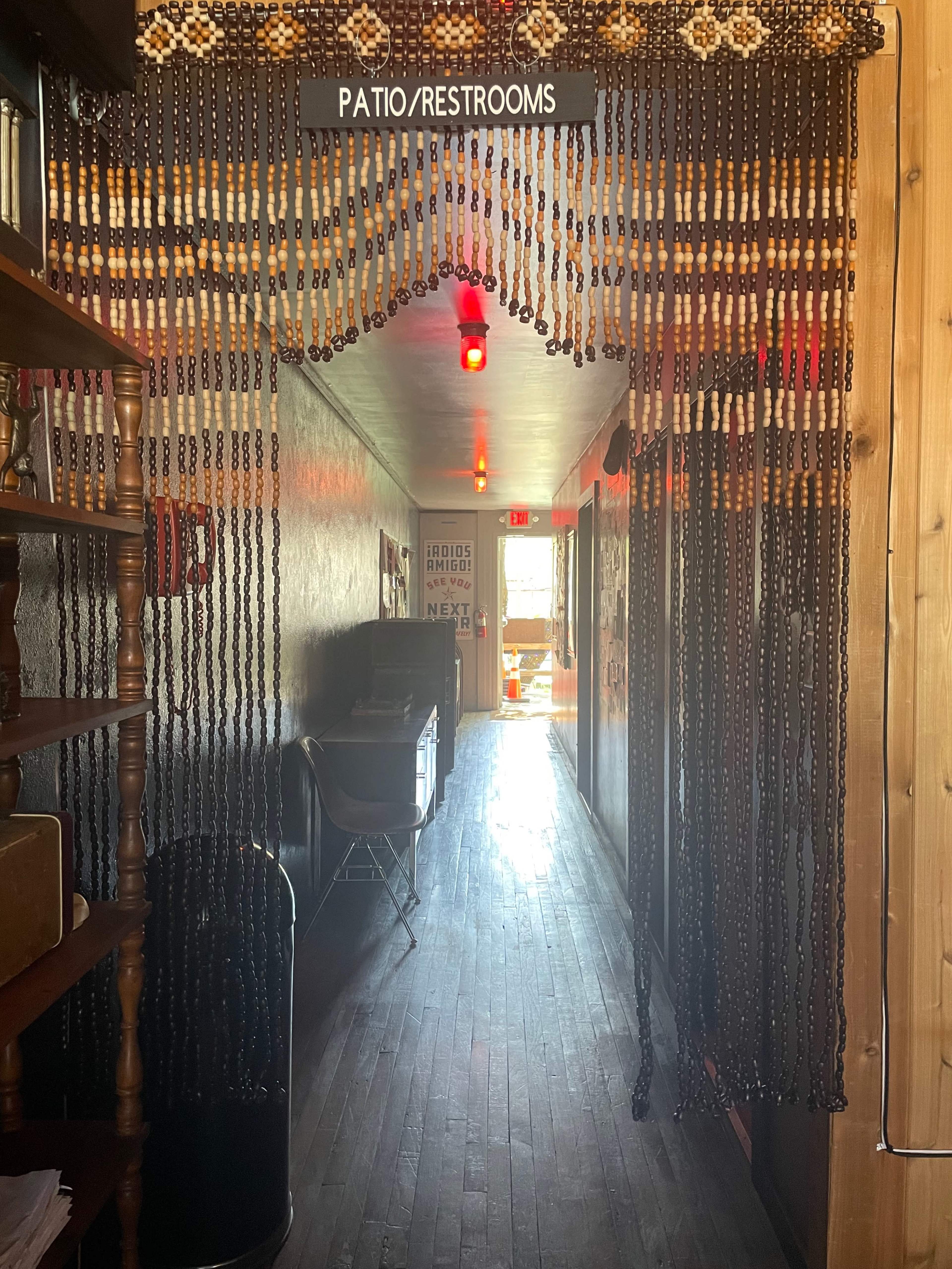 A narrow hallway features a beaded curtain leading to doorways labeled "PATIO/RESTROOMS," with wooden accents and dark flooring.