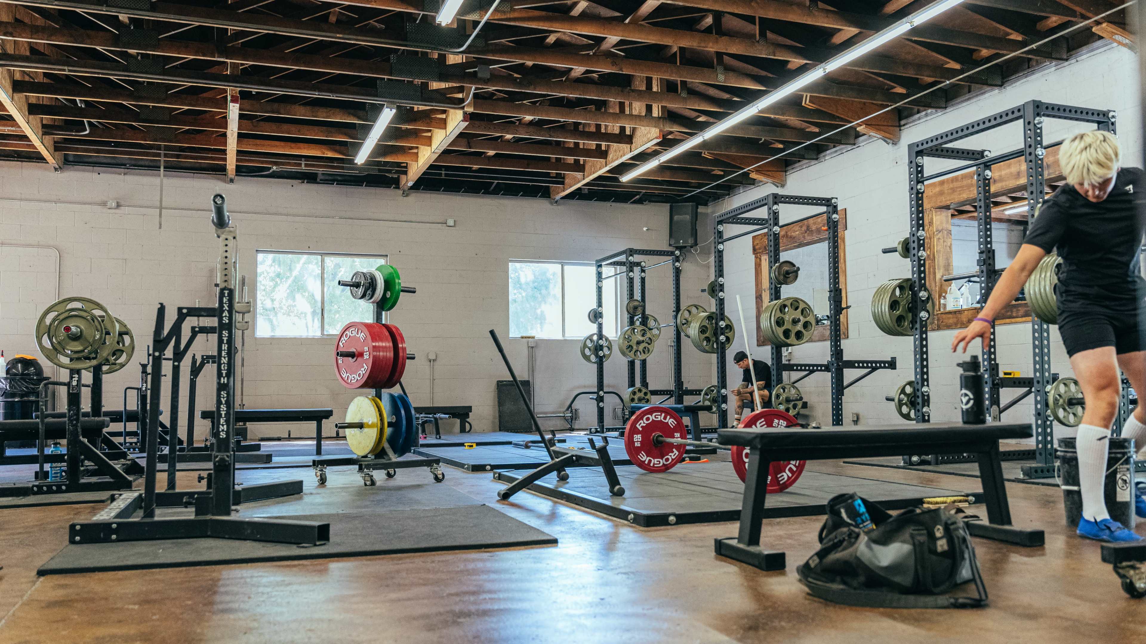 A weightlifting gym with several racks of weights, benches, and various exercise equipment in a spacious, well-lit area.