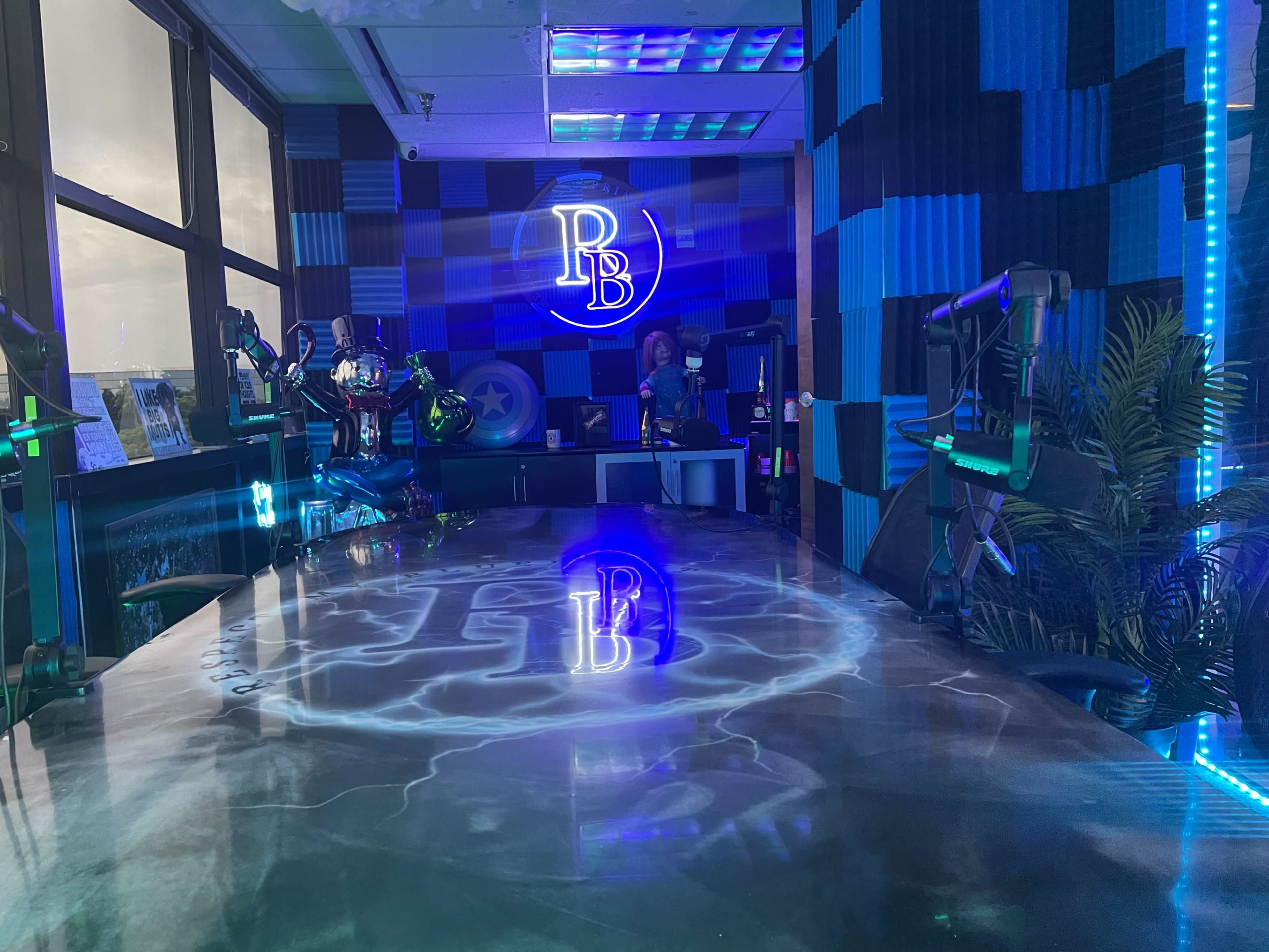A modern broadcasting studio with a large table featuring a glowing logo, surrounded by colorful lighting and equipment for video production.
