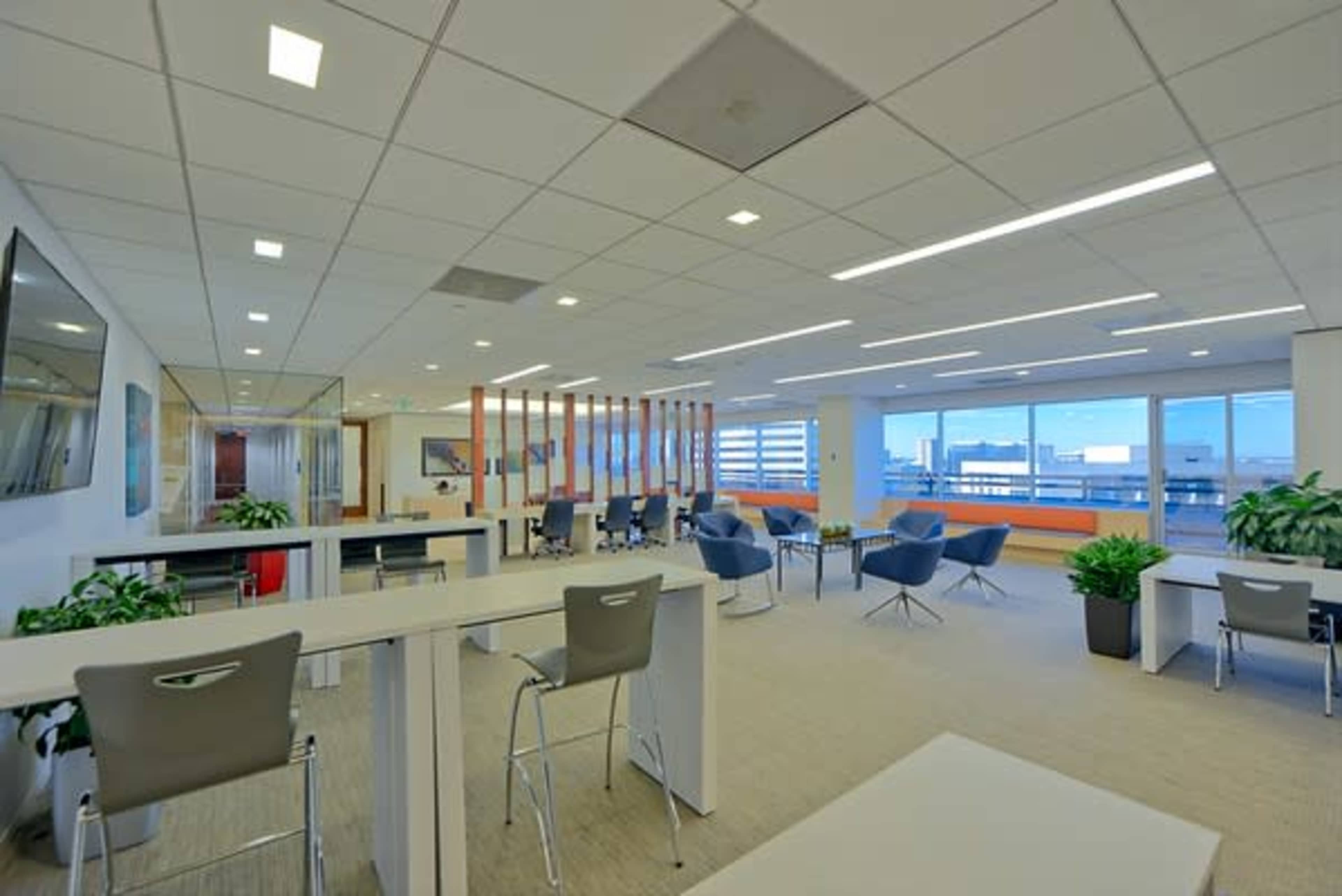 A modern office space with a mix of work areas, seating arrangements, and large windows overlooking a cityscape.