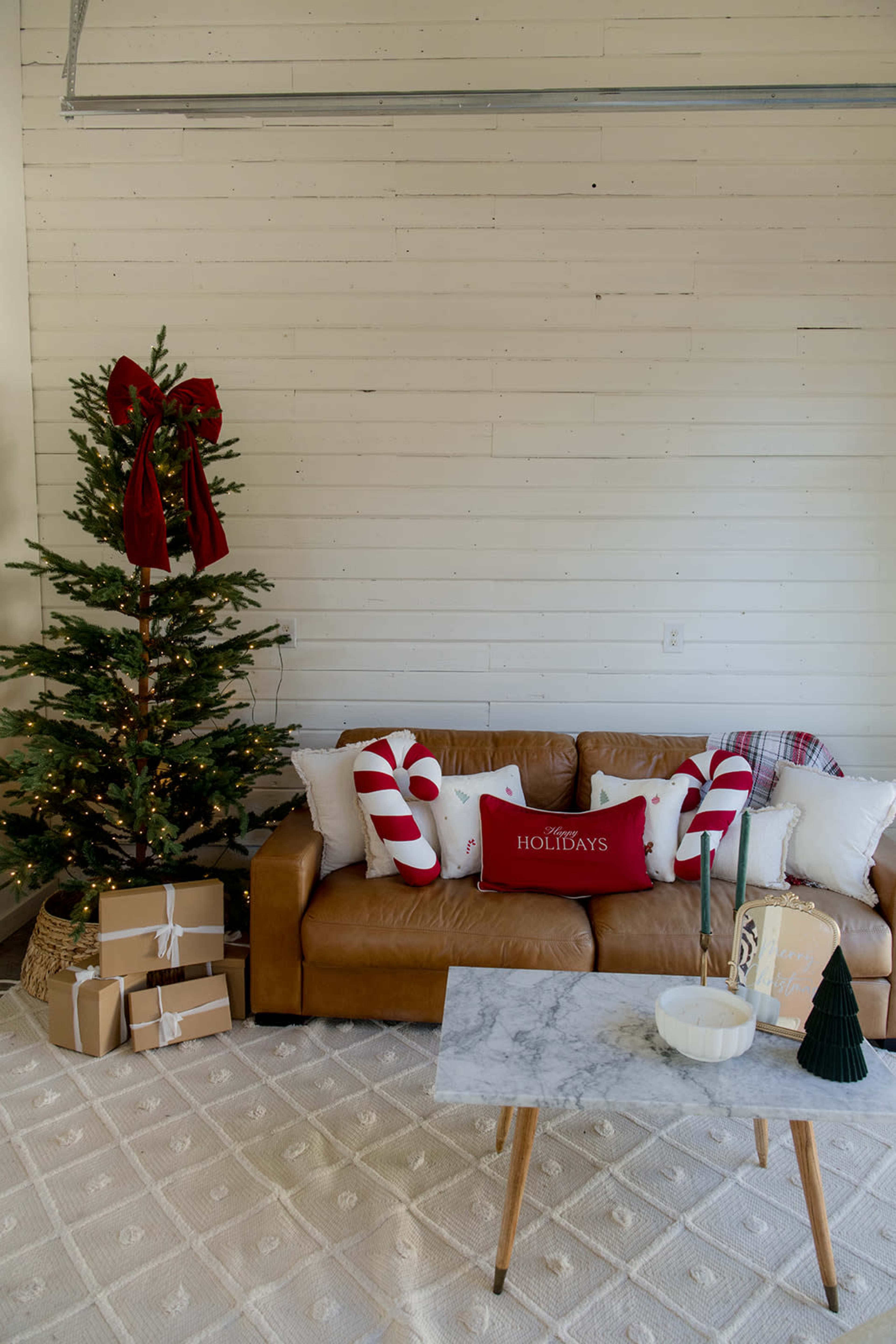 The image shows a cozy living room decorated for the holidays, featuring a Christmas tree, a brown leather couch with festive pillows, and a marble coffee table with holiday-themed decor.