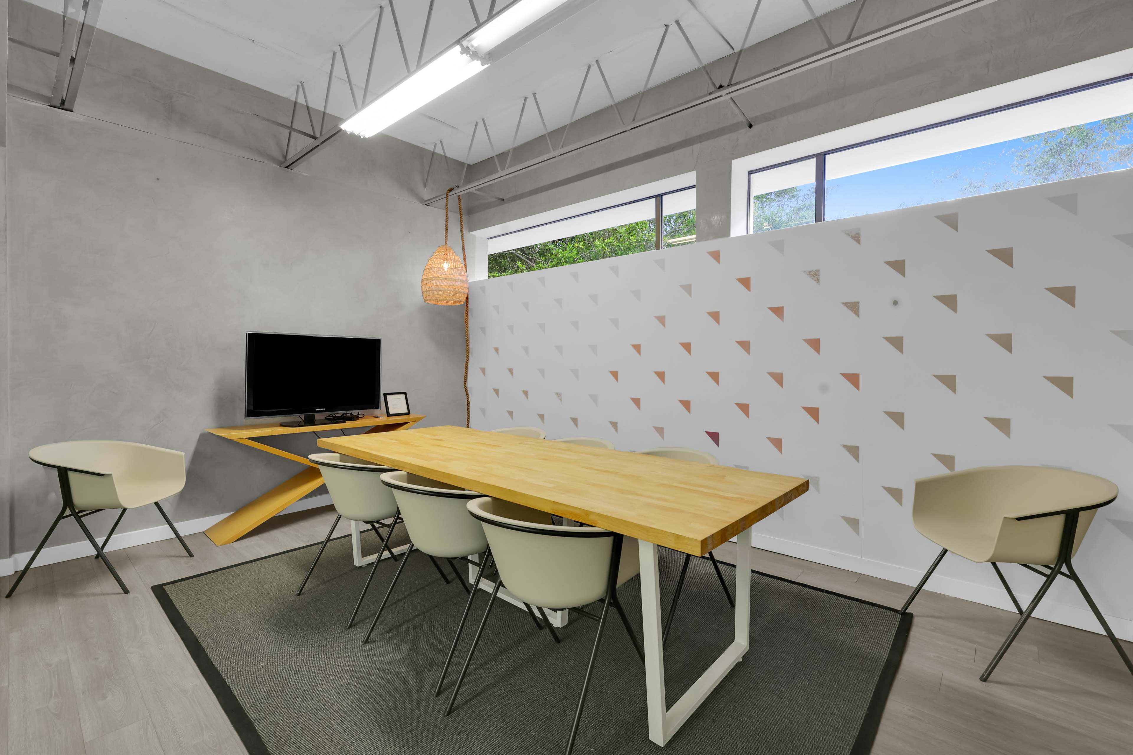 A modern conference room features a wooden table with five chairs, a television mounted on the wall, and a geometric partition.