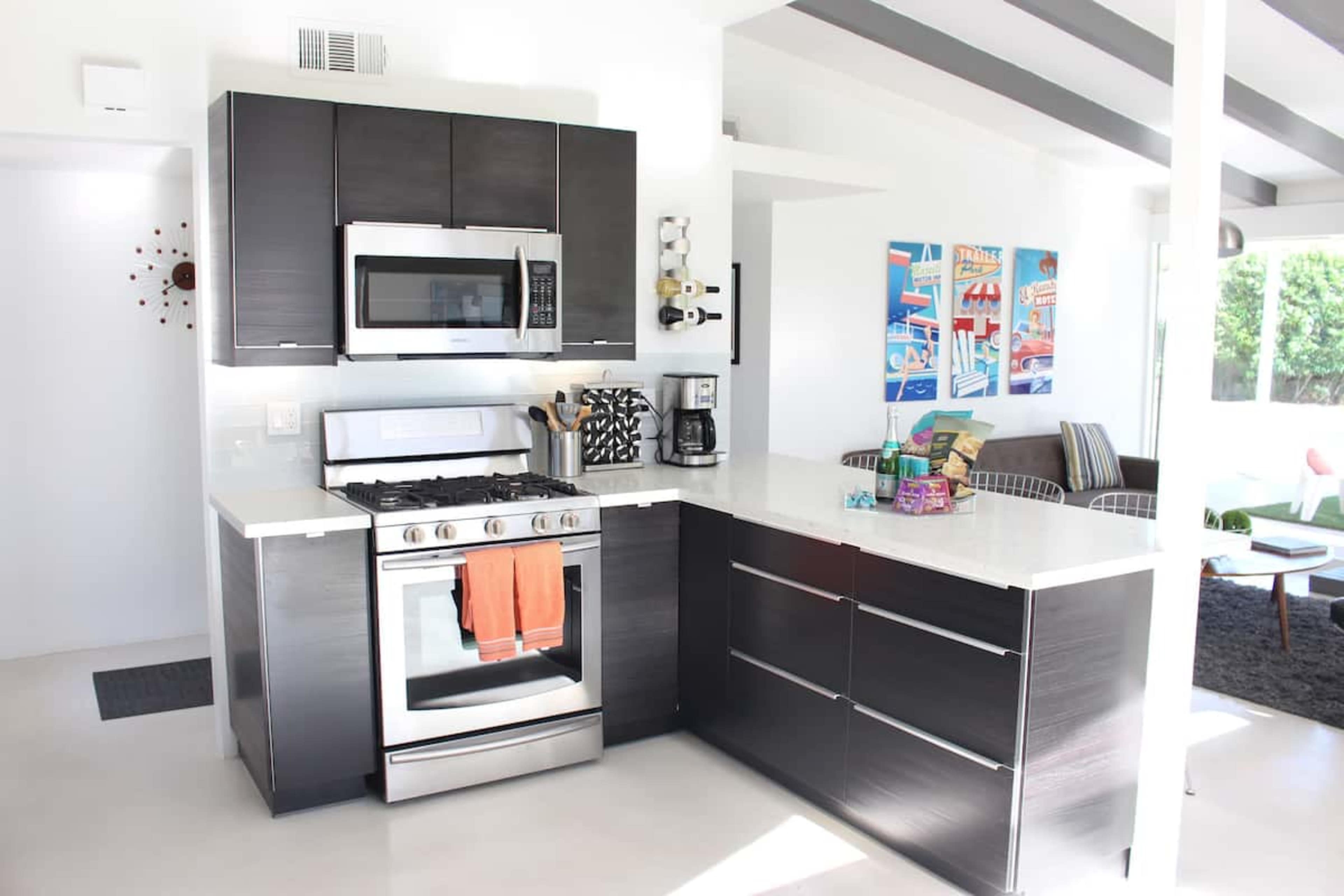 The image shows a modern kitchen with dark cabinetry, stainless steel appliances, and a marble countertop.