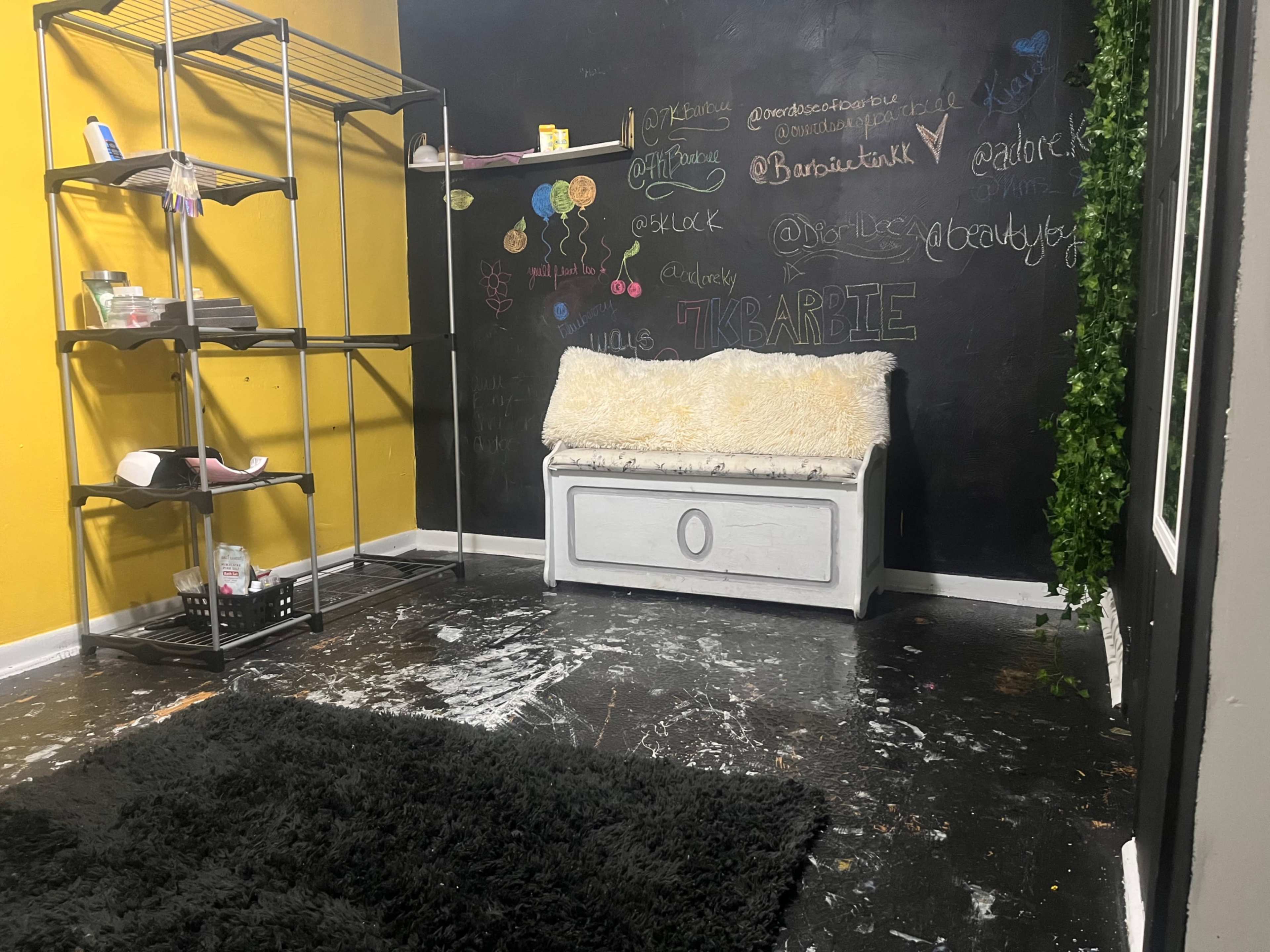 A small room with a black wall covered in chalkboard writing, a white couch with a fuzzy throw, and a metal shelving unit against the wall.