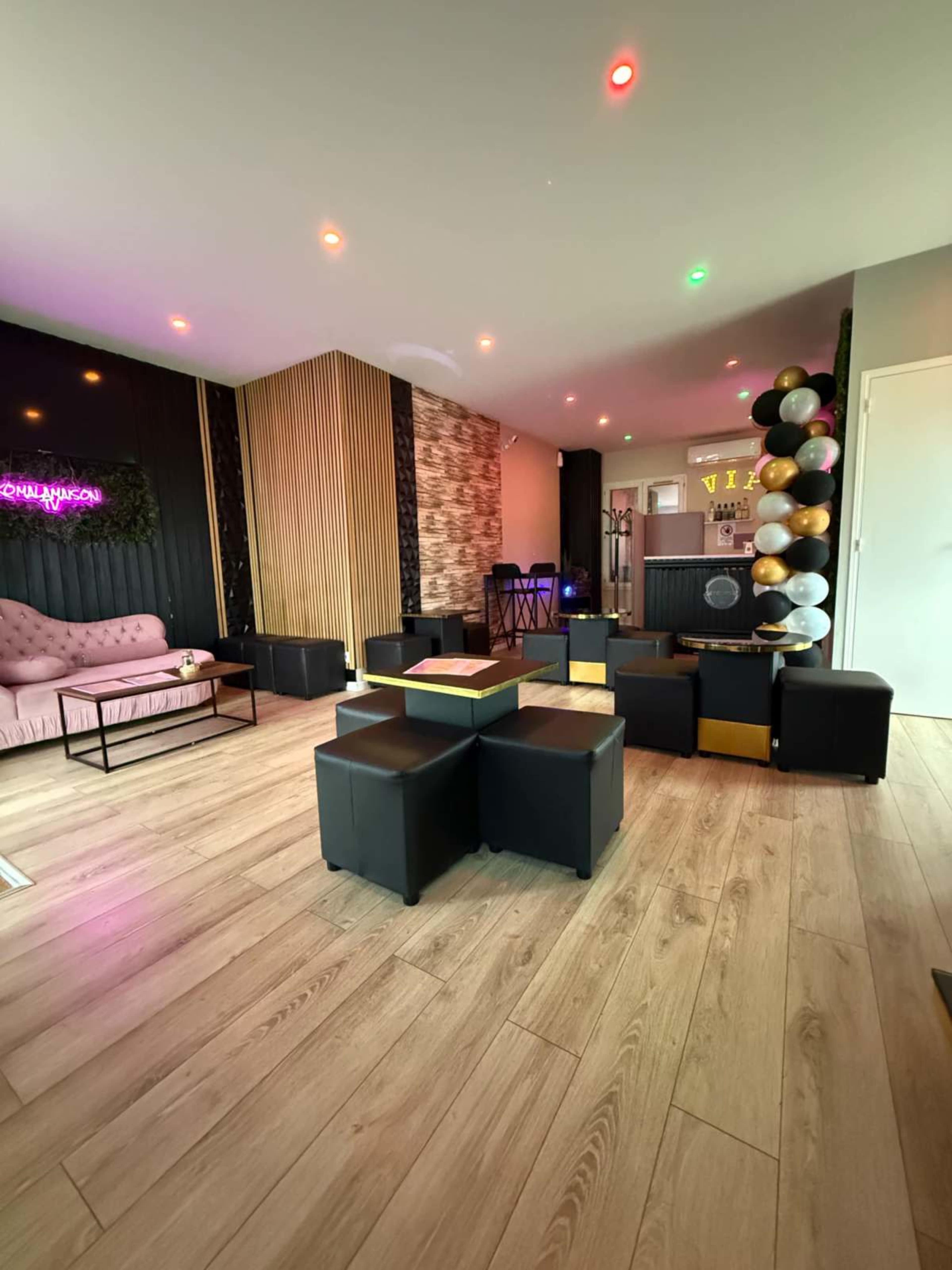 The image shows a modern lounge space with a pink sofa, black cube seating, and decorative balloons in a corner.