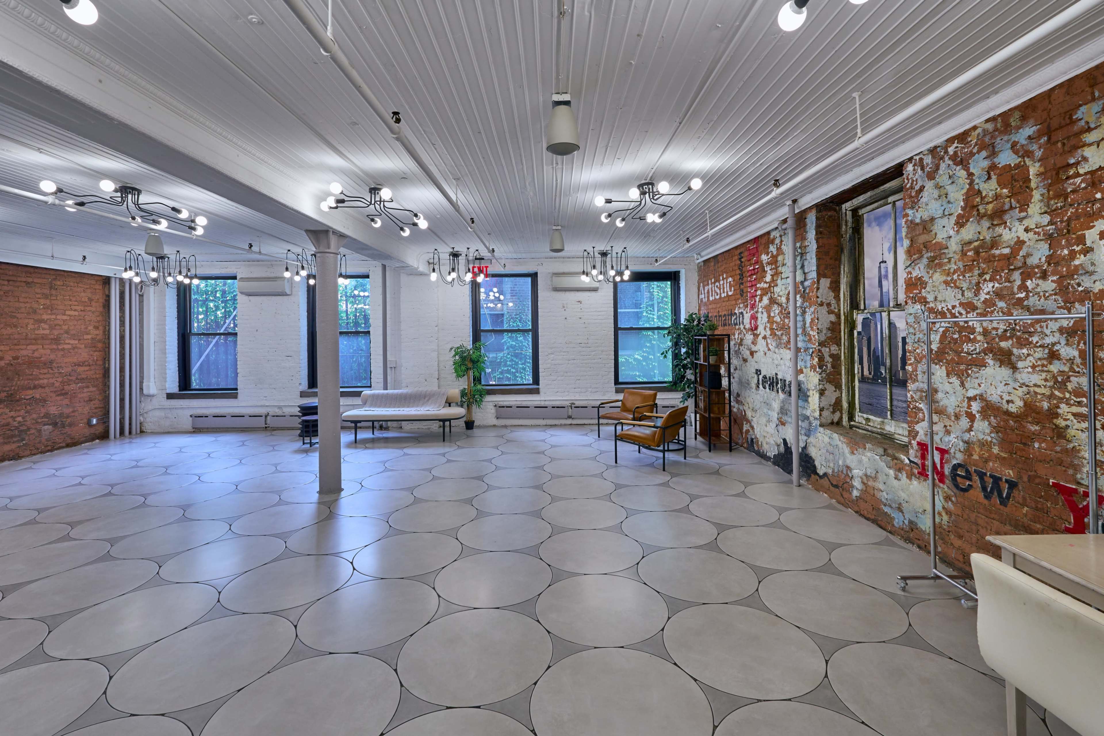 A spacious, empty room with brick walls, large windows, and a tiled floor arranged in an attractive pattern.