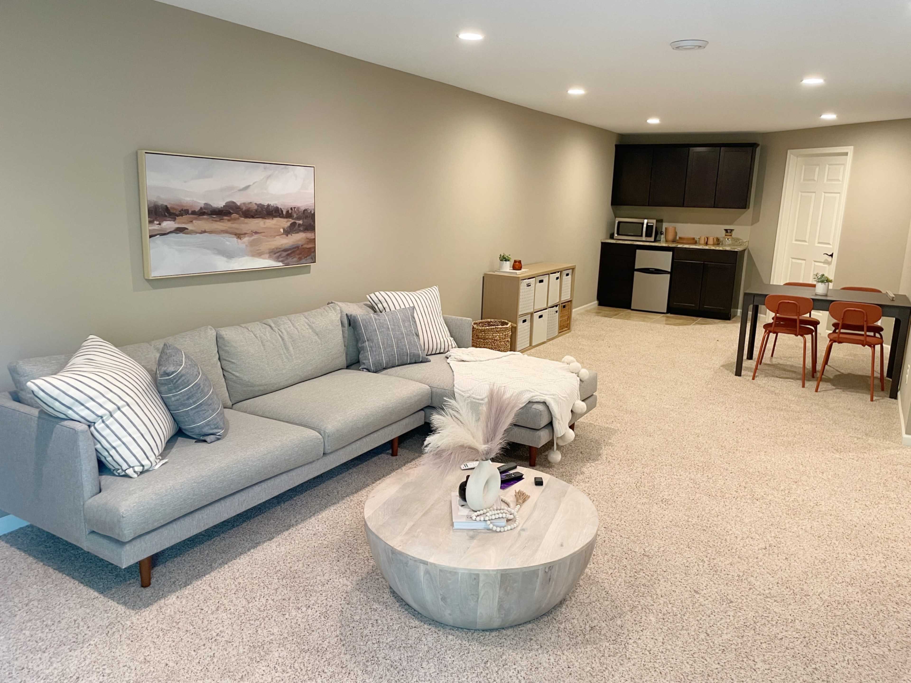 A cozy living area with a gray sectional sofa, a round coffee table, and a dining area featuring a small table with chairs, set against a light-colored wall.