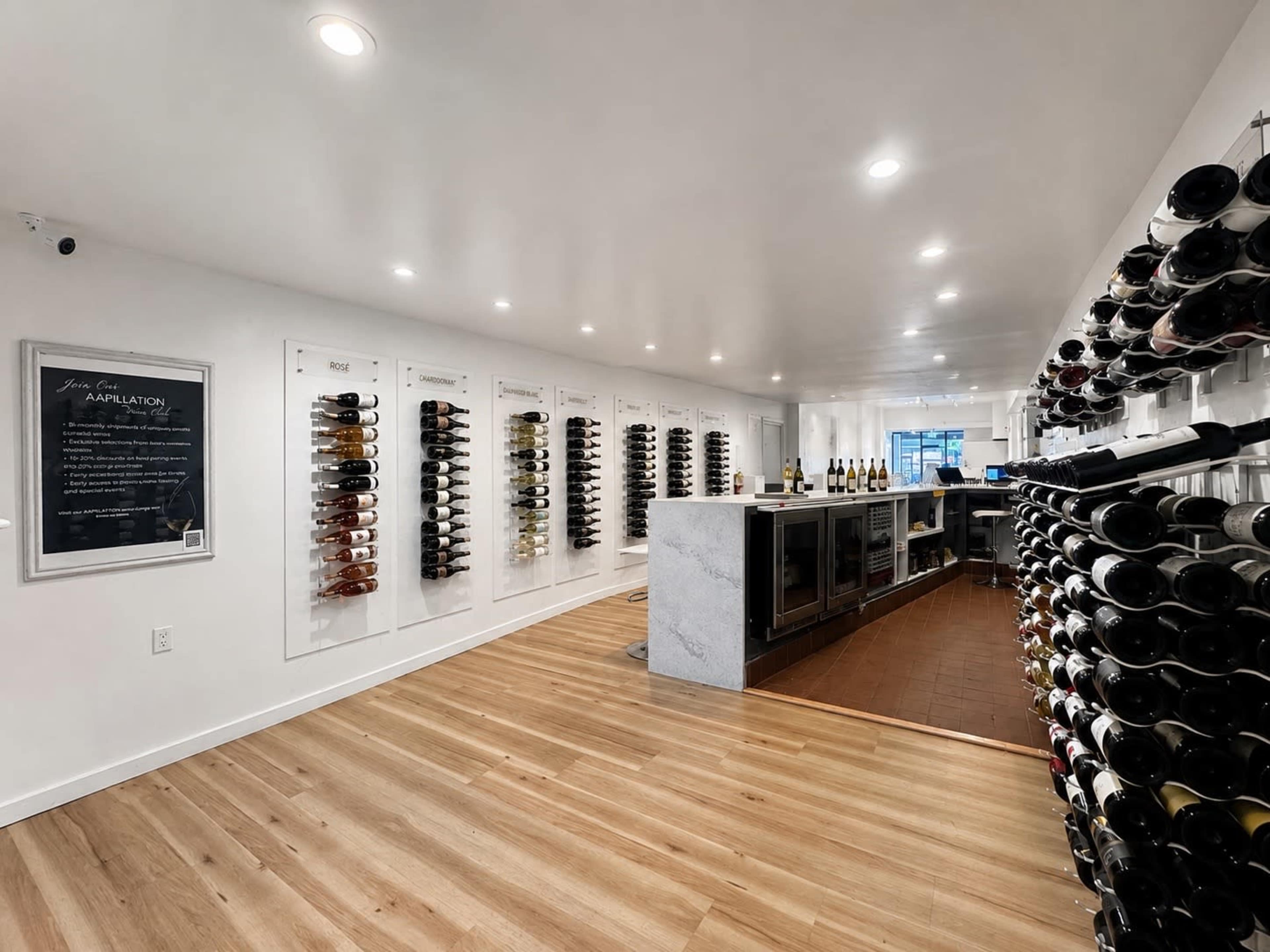 The image shows a sleek wine tasting room with wine bottles displayed on walls and a central bar area.