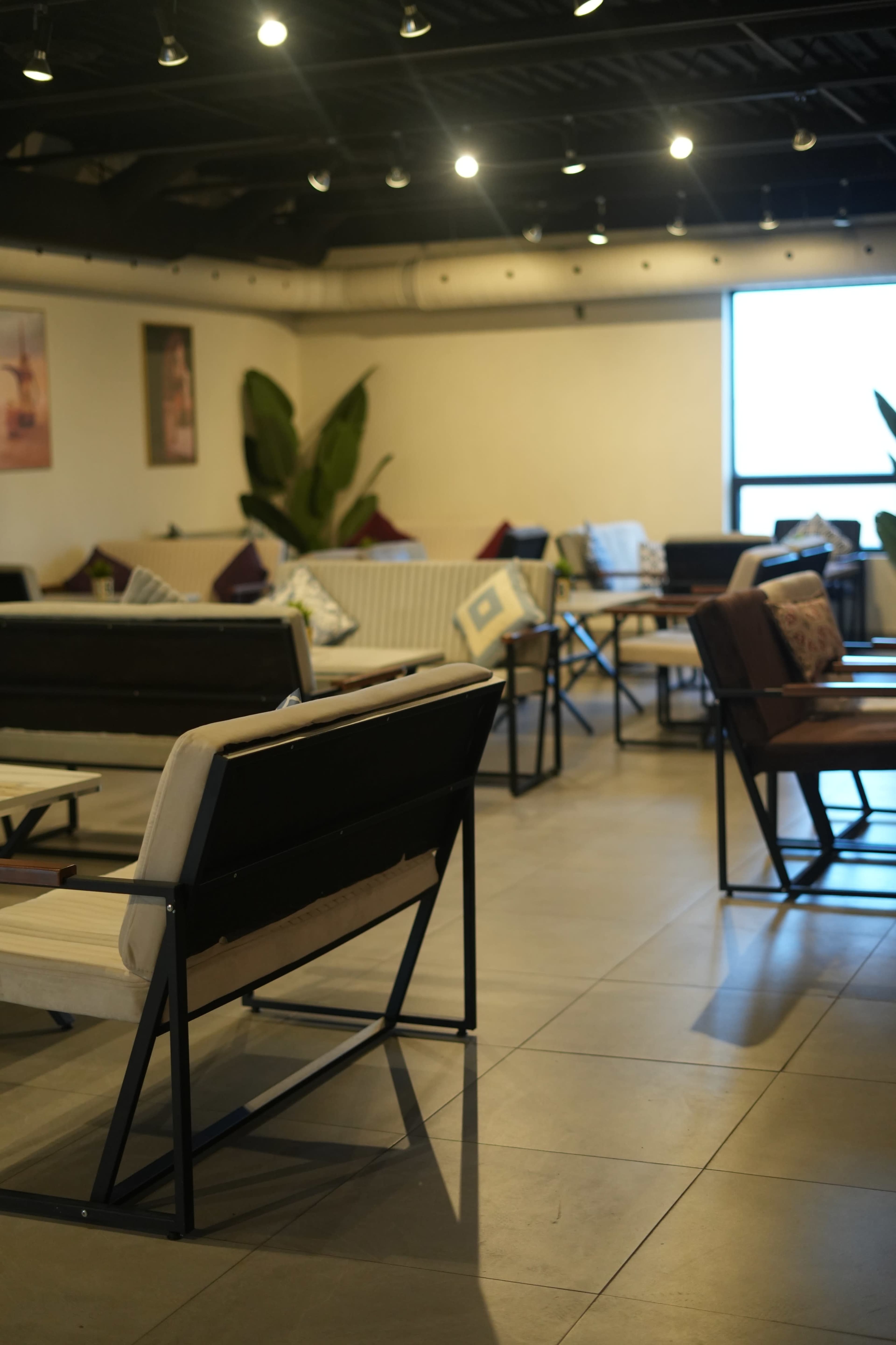 The image shows a modern, spacious lounge area with several tables and chairs arranged around a large window.