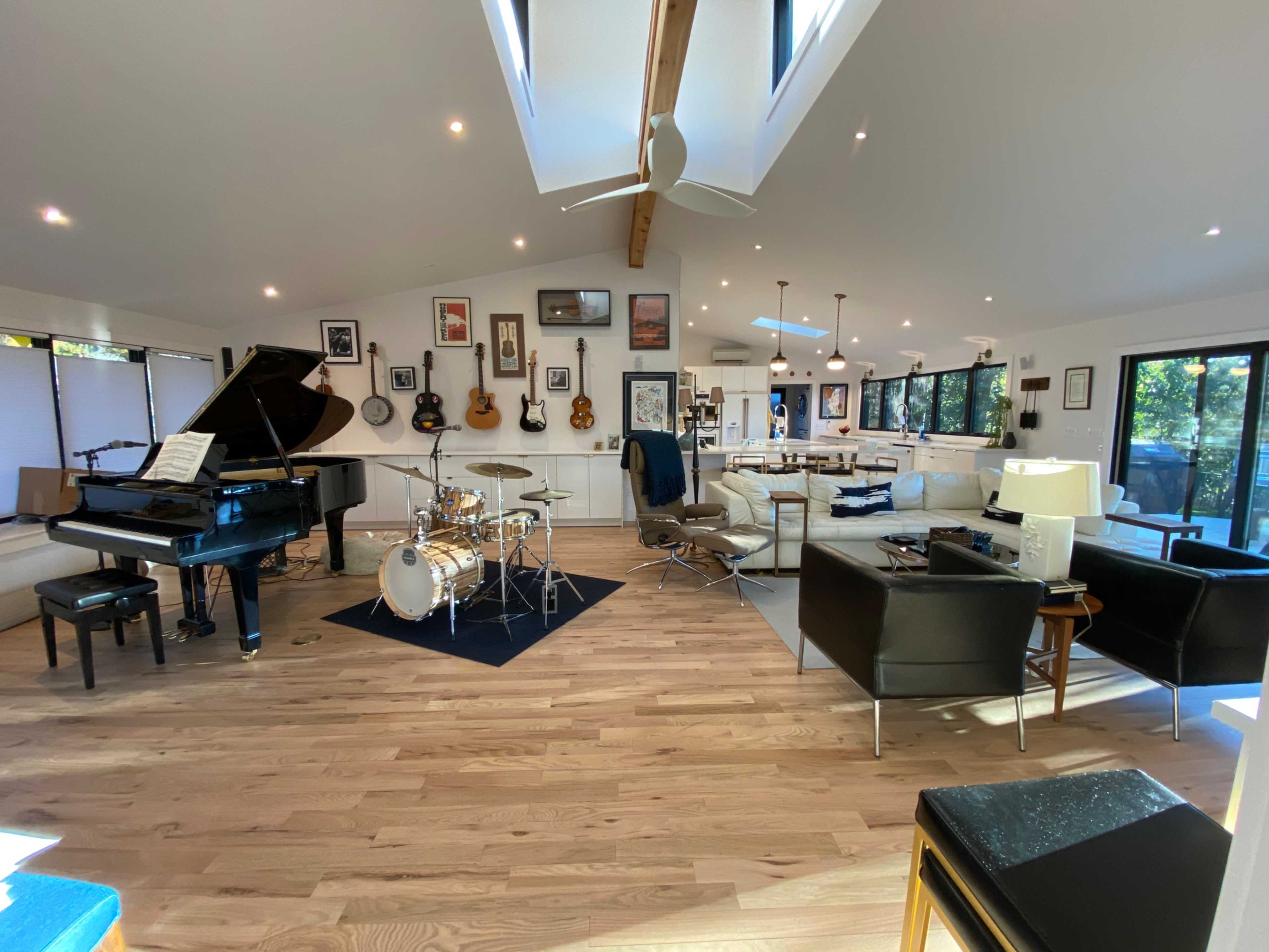 The image shows a spacious, modern living area with a grand piano, a drum set, and various framed artworks on the walls.