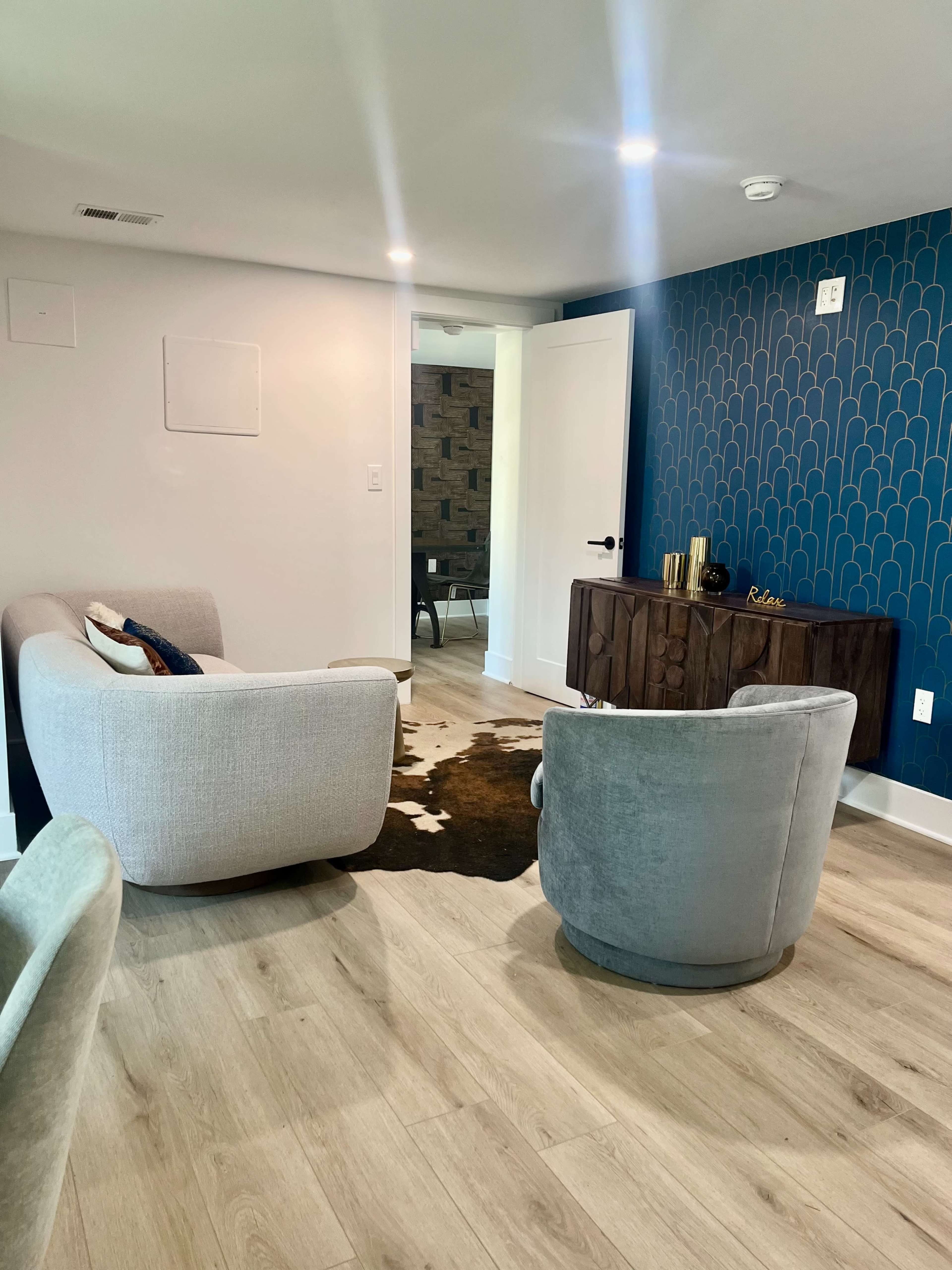 A modern living space featuring two upholstered chairs, a wall with a blue patterned design, and a wooden sideboard with decorative items.