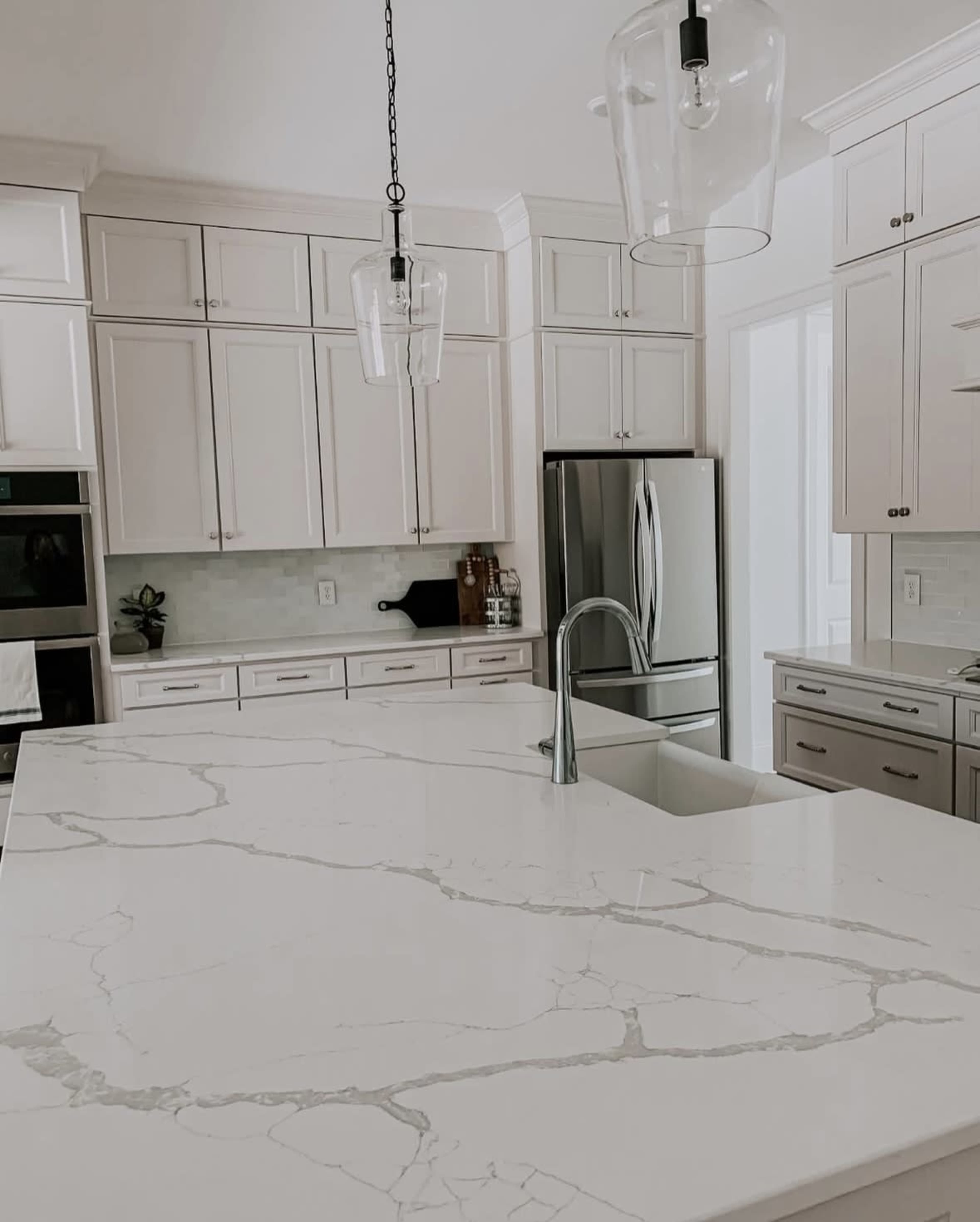 The image shows a modern kitchen featuring a large marble island, stainless steel appliances, and white cabinetry with under-cabinet lighting.