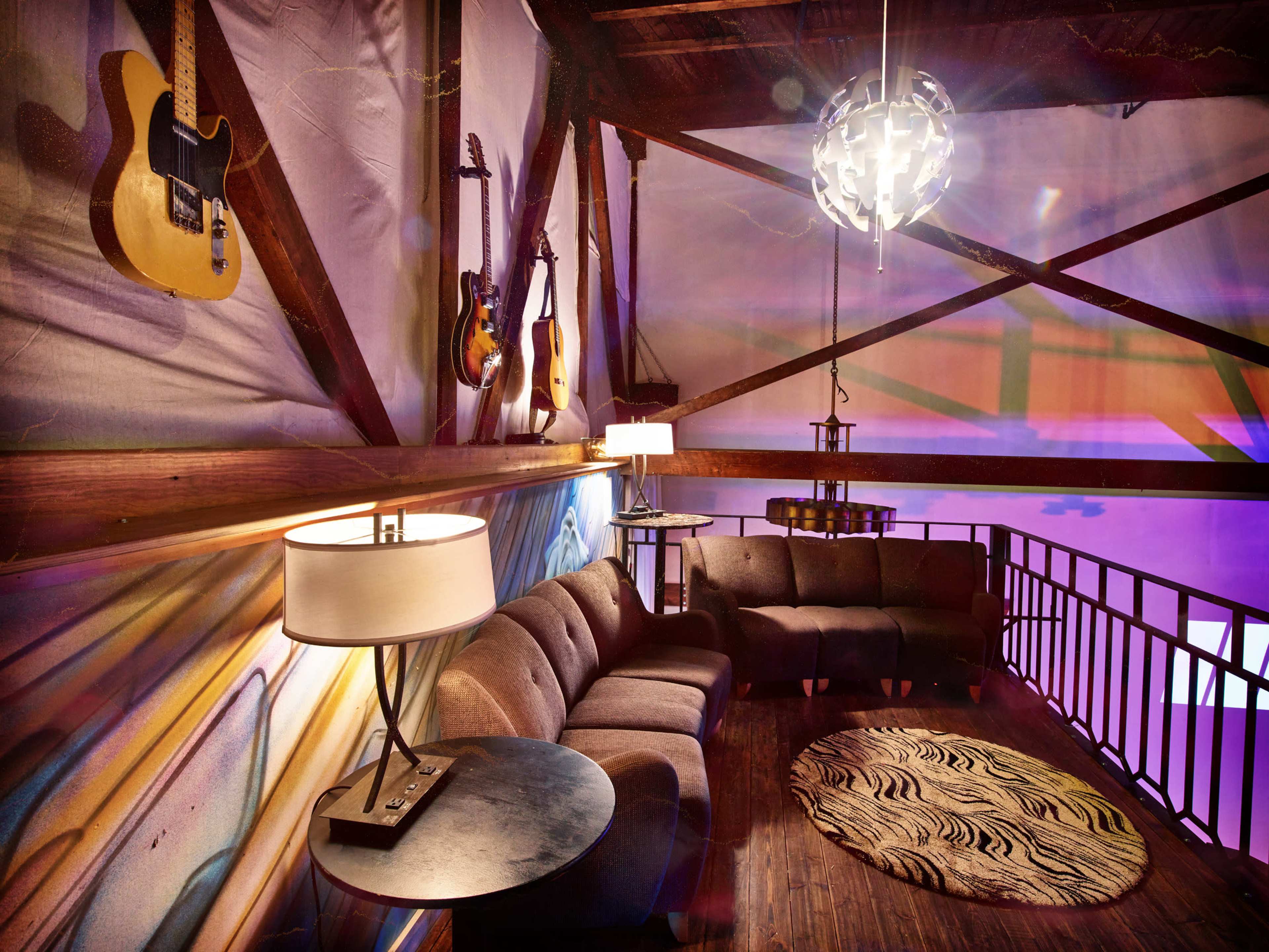 A cozy lounge area with a curved sofa, a round rug, and guitars displayed on the walls, illuminated by modern lighting fixtures.