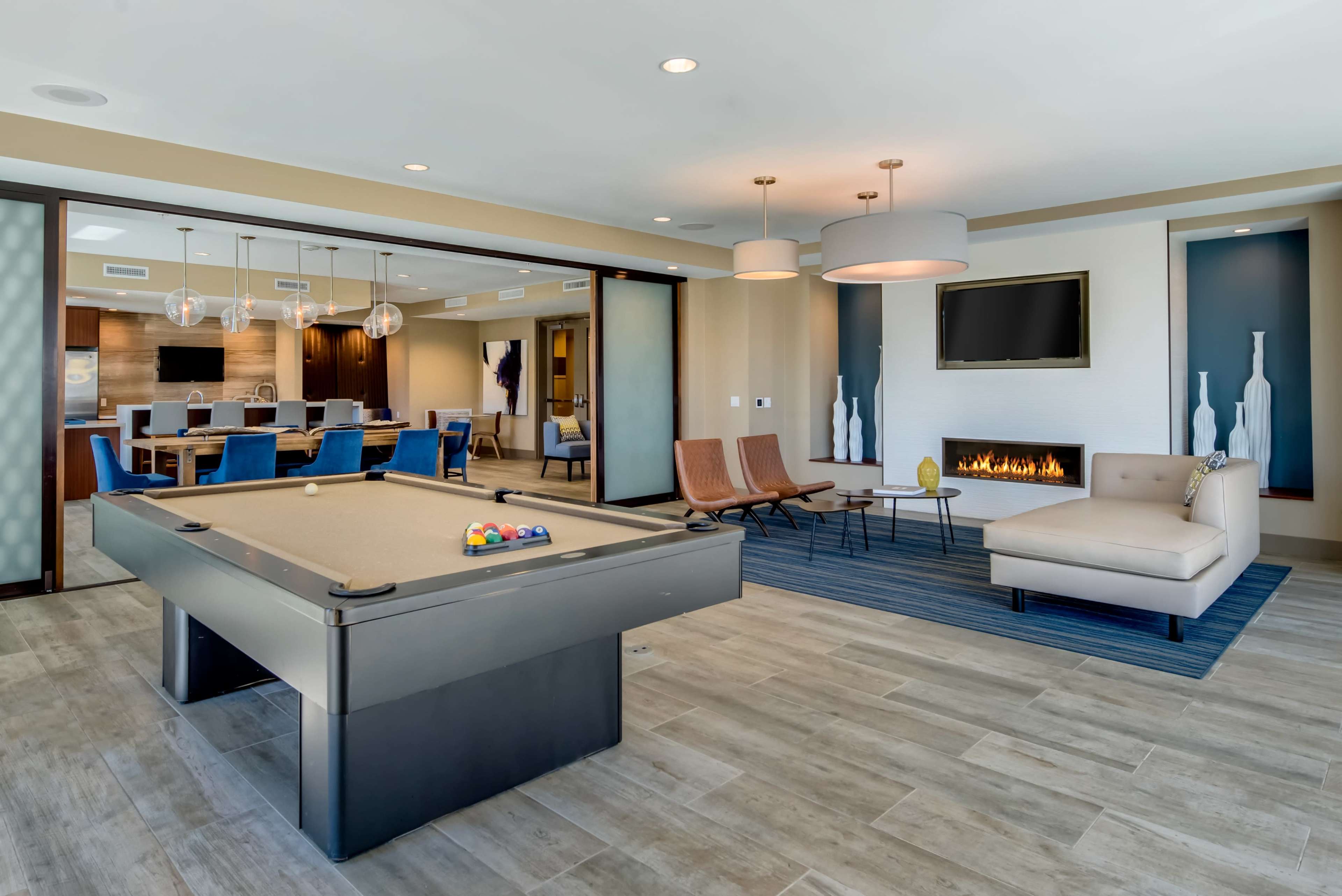 A modern lounge area featuring a pool table, seating arrangements, and a fireplace, with a large meeting room visible in the background.