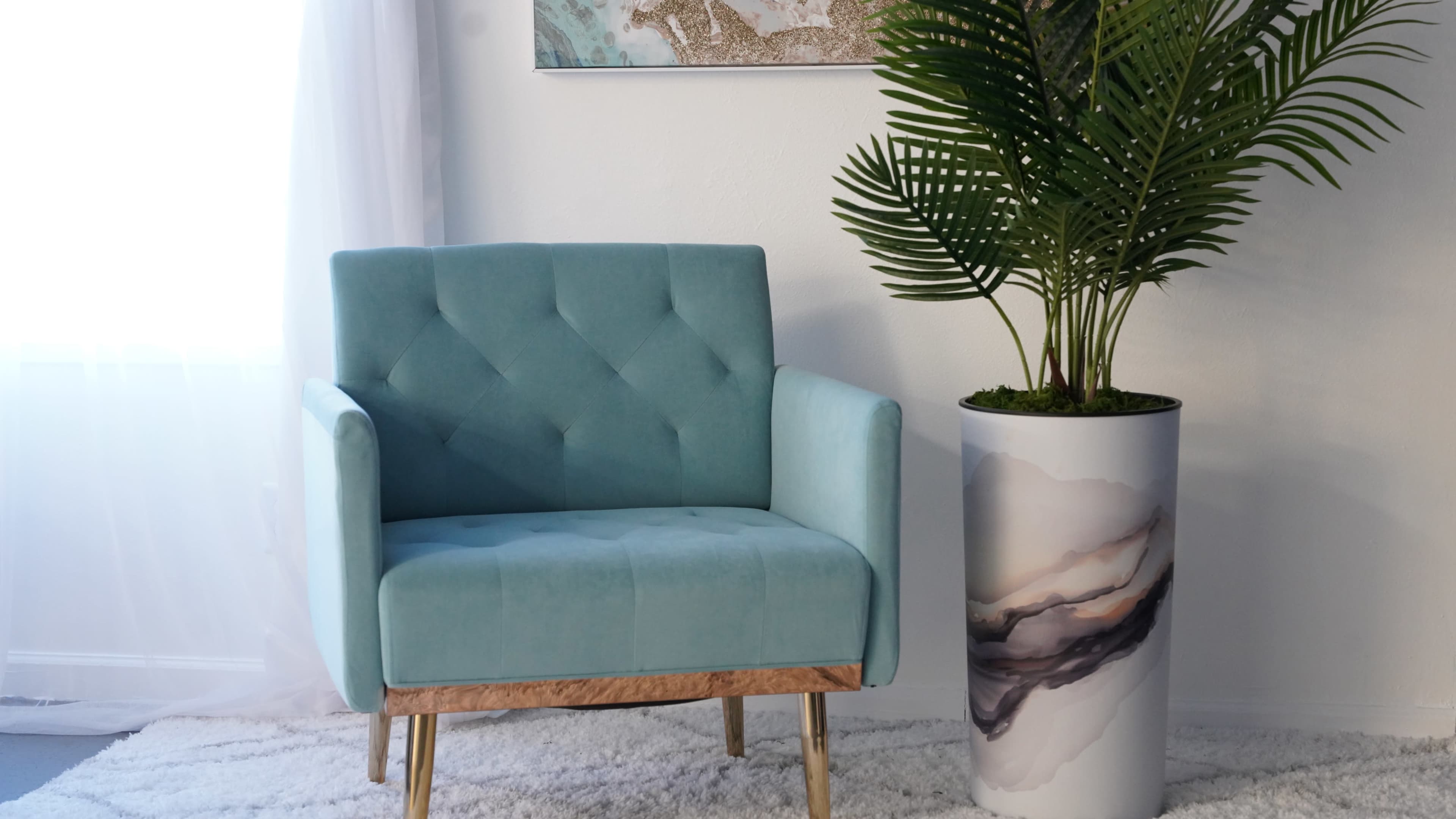 A light blue upholstered chair with a tufted design sits beside a large decorative planter containing a leafy plant, on a textured rug in a well-lit room.