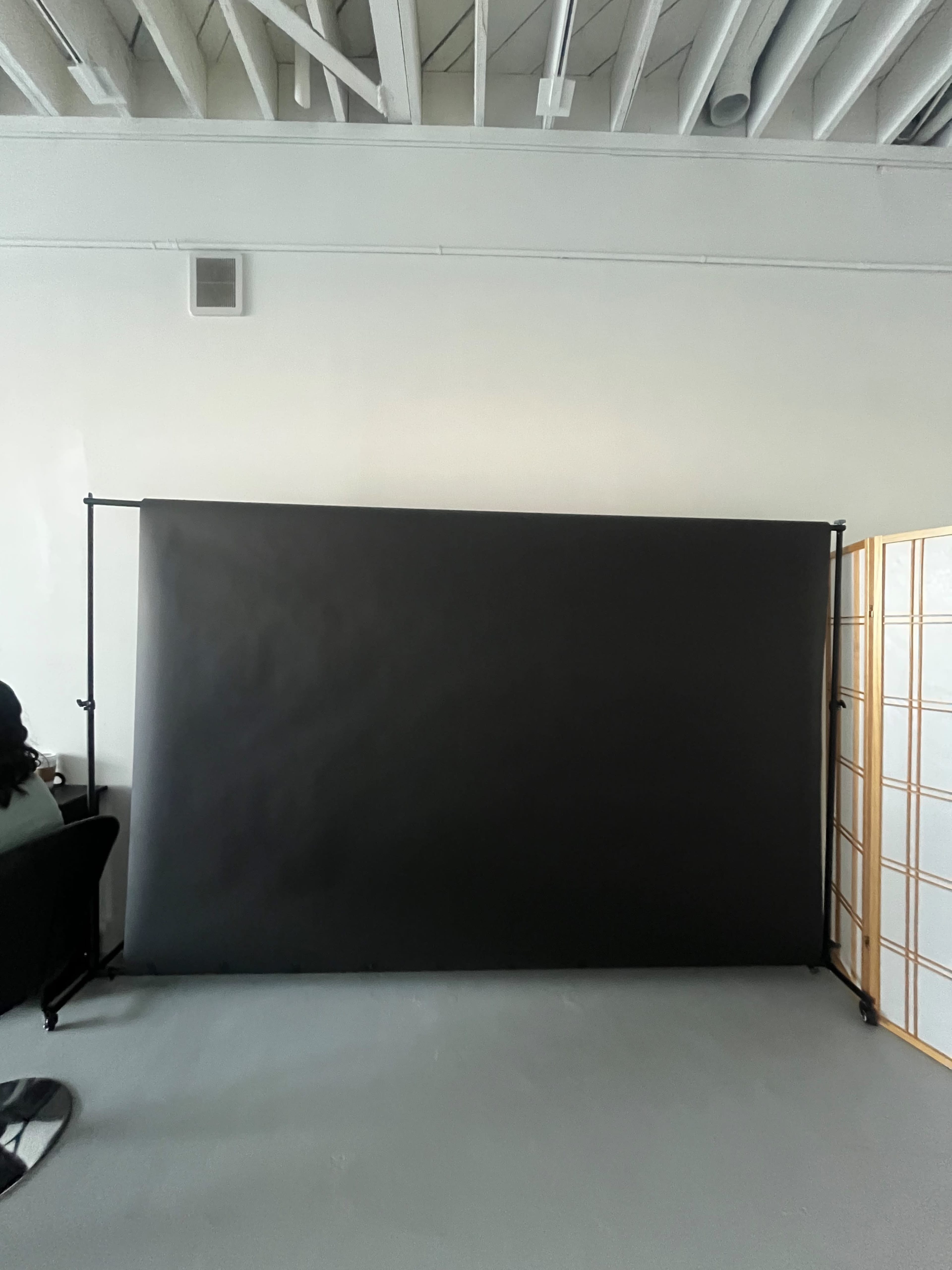 The image shows a black backdrop set up on a frame against a plain light-colored wall in a spacious room.