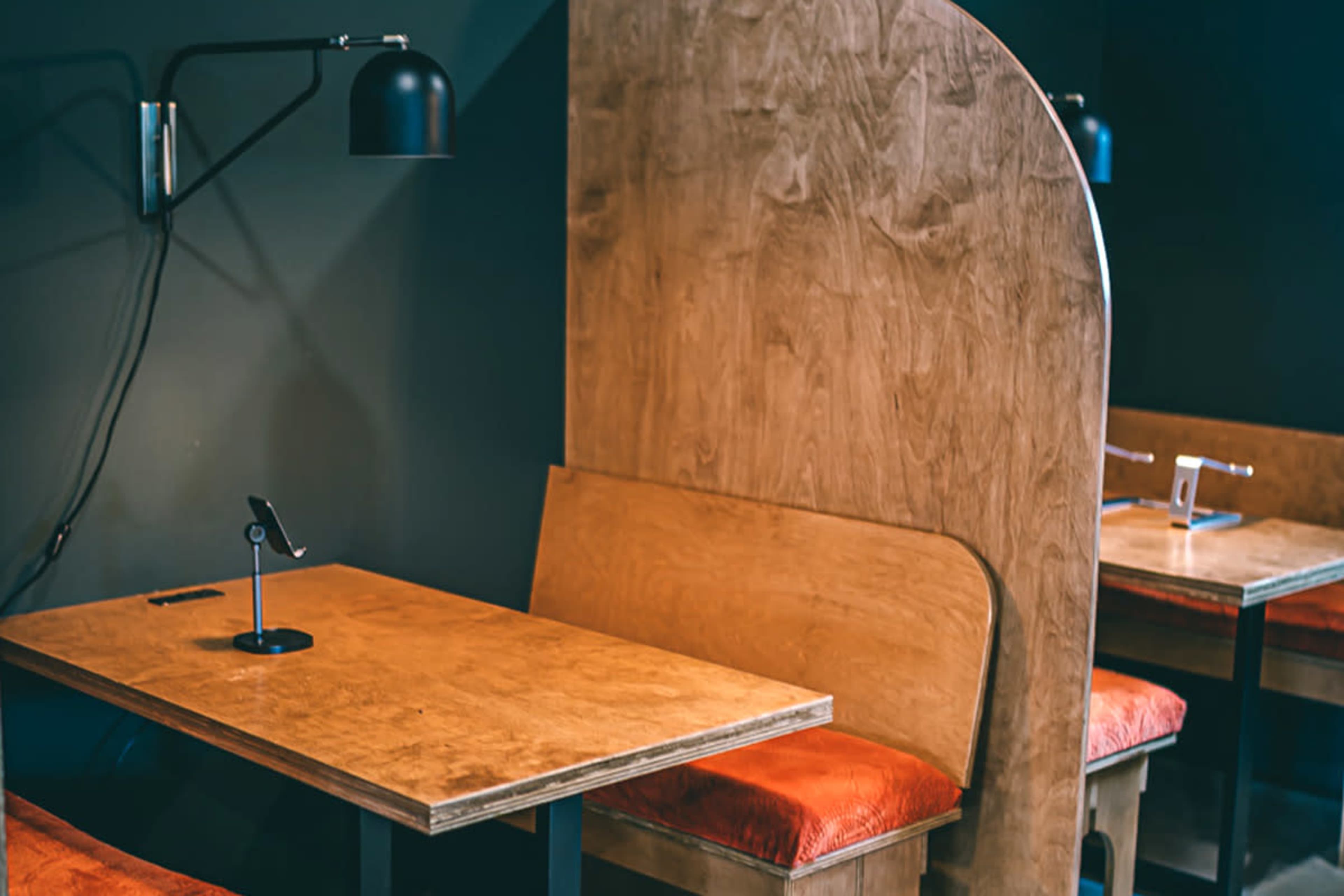 A minimalist café interior with wooden booths, tables, and a black lamp illuminating the space.