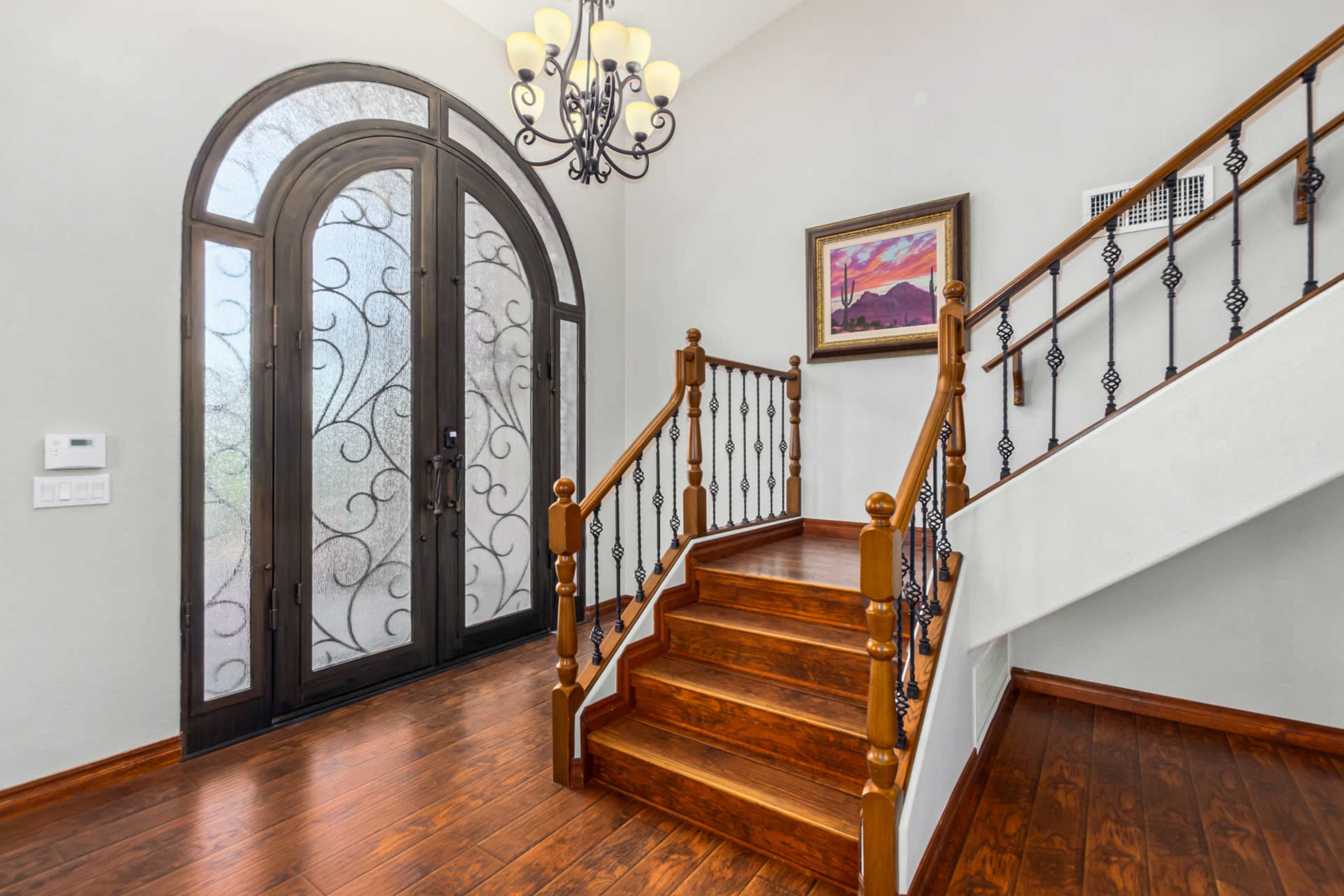 An entrance hallway with a wooden staircase and a large, arched front door featuring intricate ironwork.