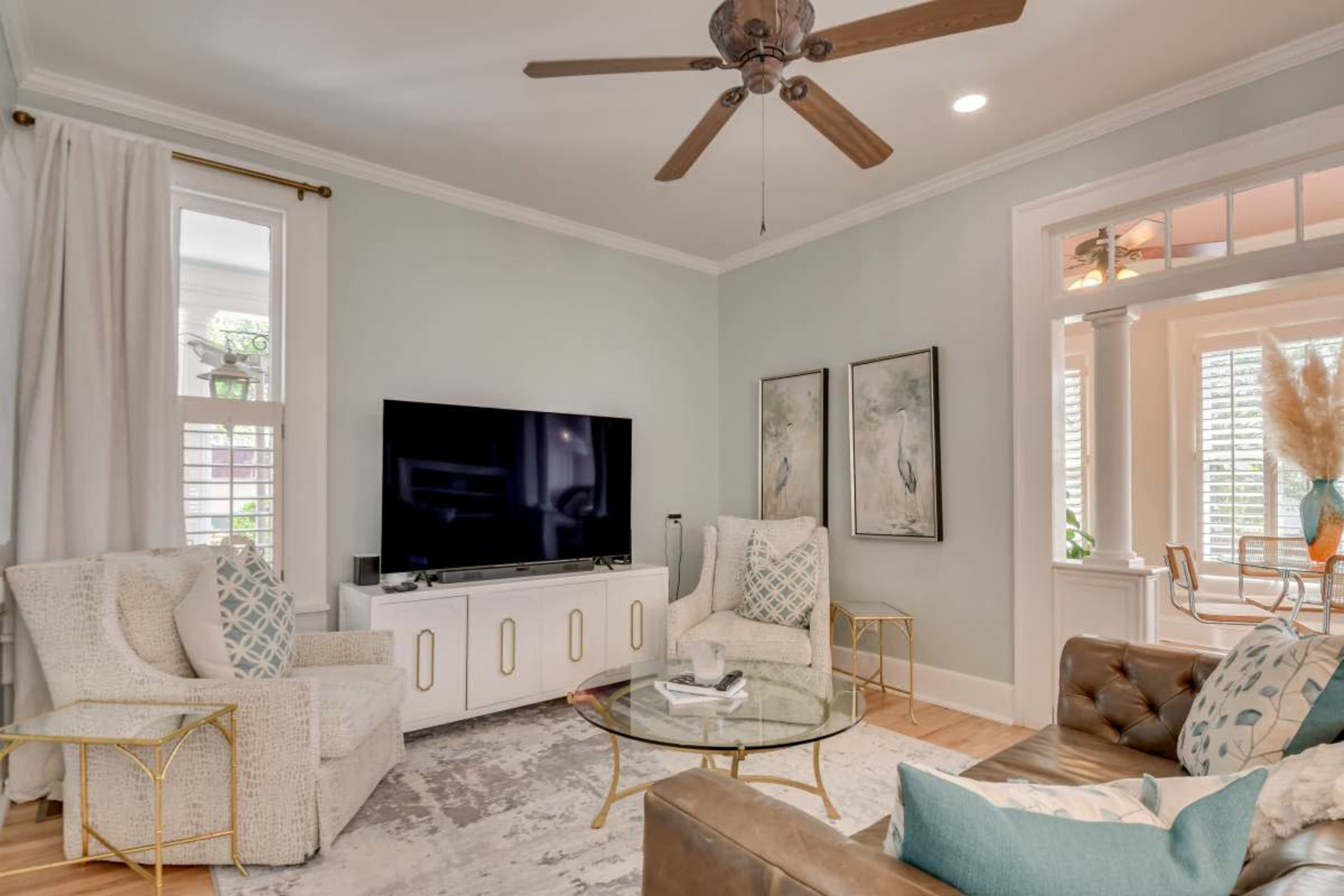 The image depicts a modern living room featuring two armchairs, a brown leather couch, a coffee table, and a large television mounted on the wall.