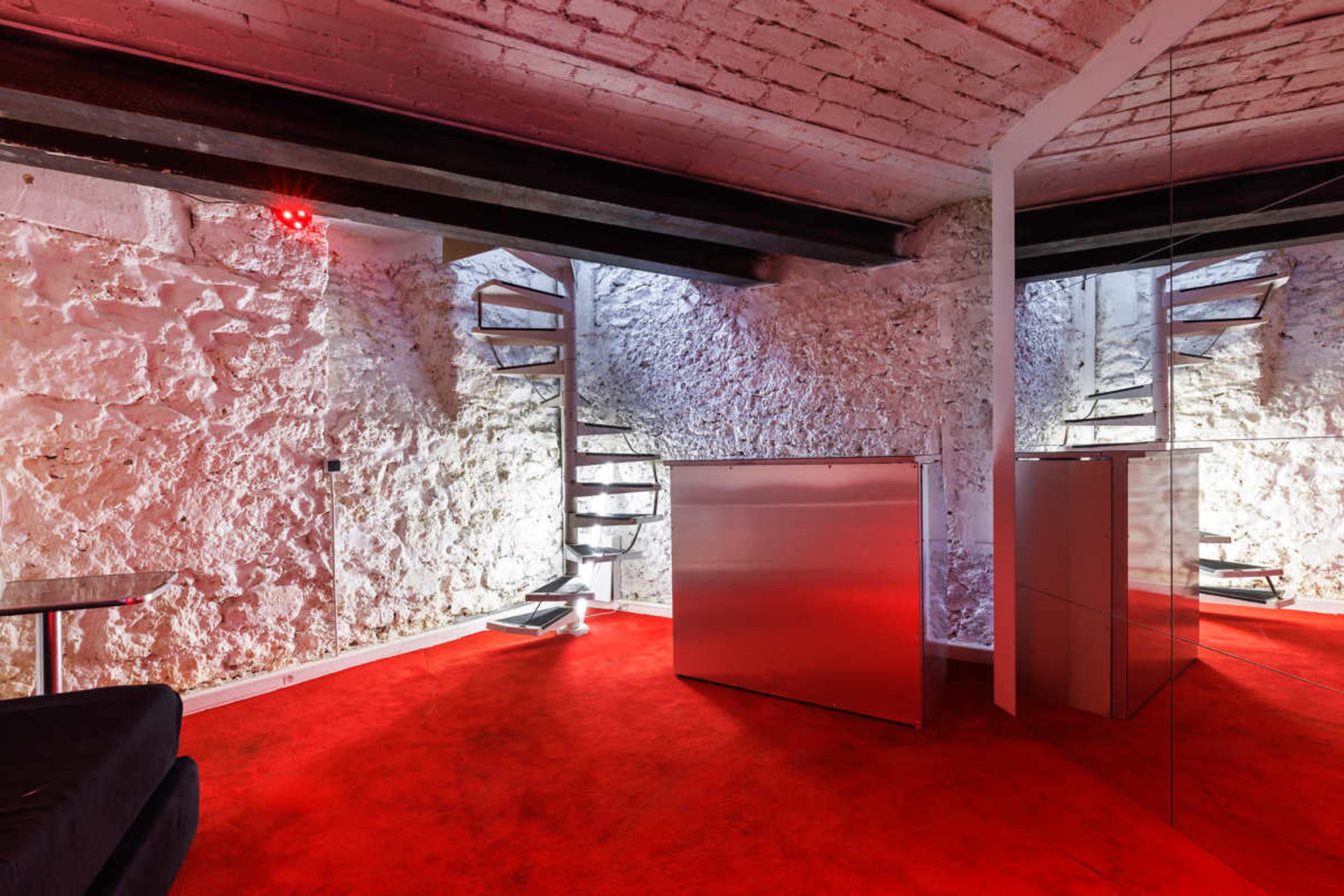 The image shows a modern, minimalist interior with red carpet and a concrete wall, featuring a spiral staircase and reflective surfaces.