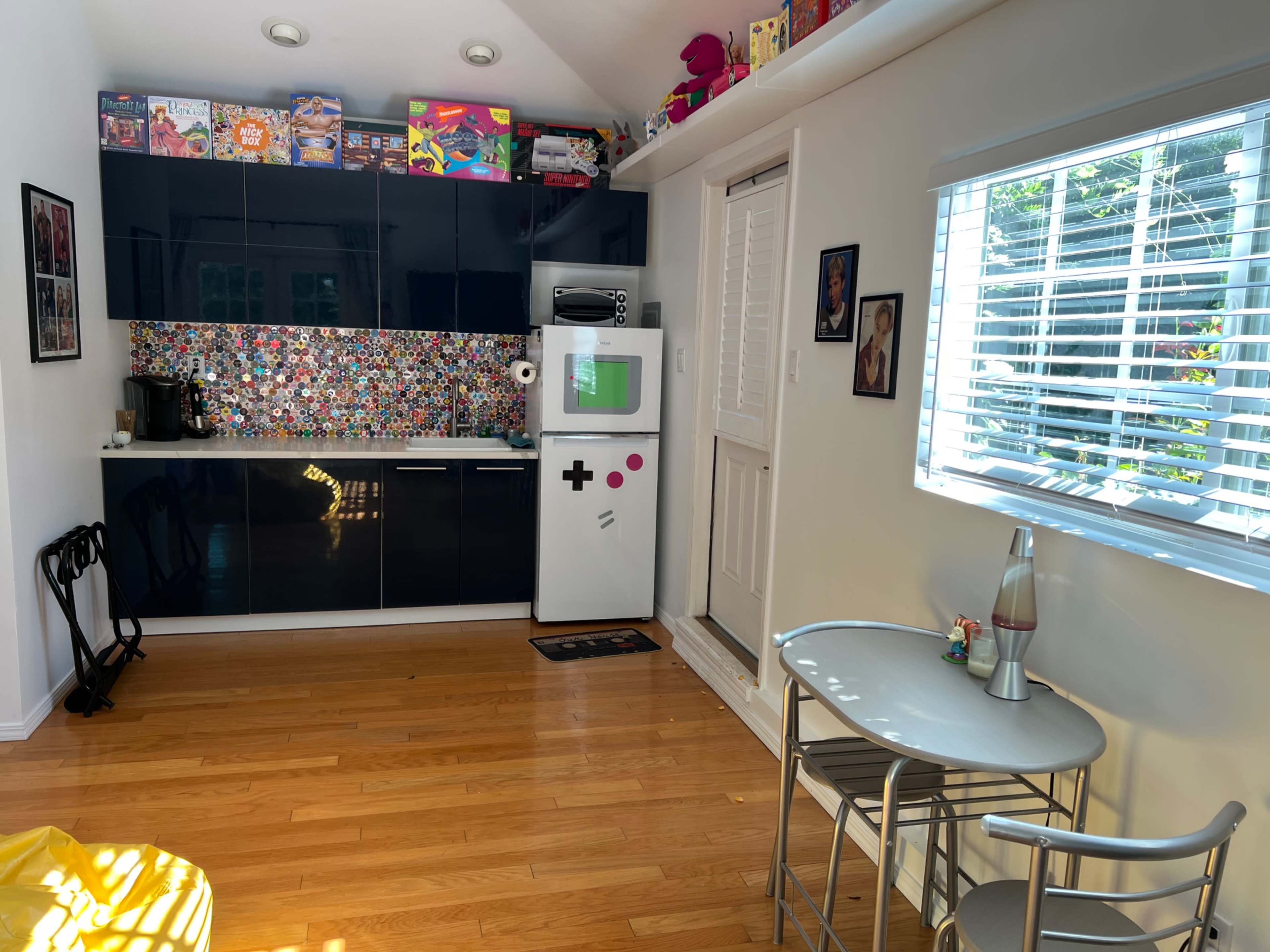 A modern kitchen area with a colorful backsplash, a white fridge with a playful design, and a small dining table set against a backdrop of natural light from a nearby window.