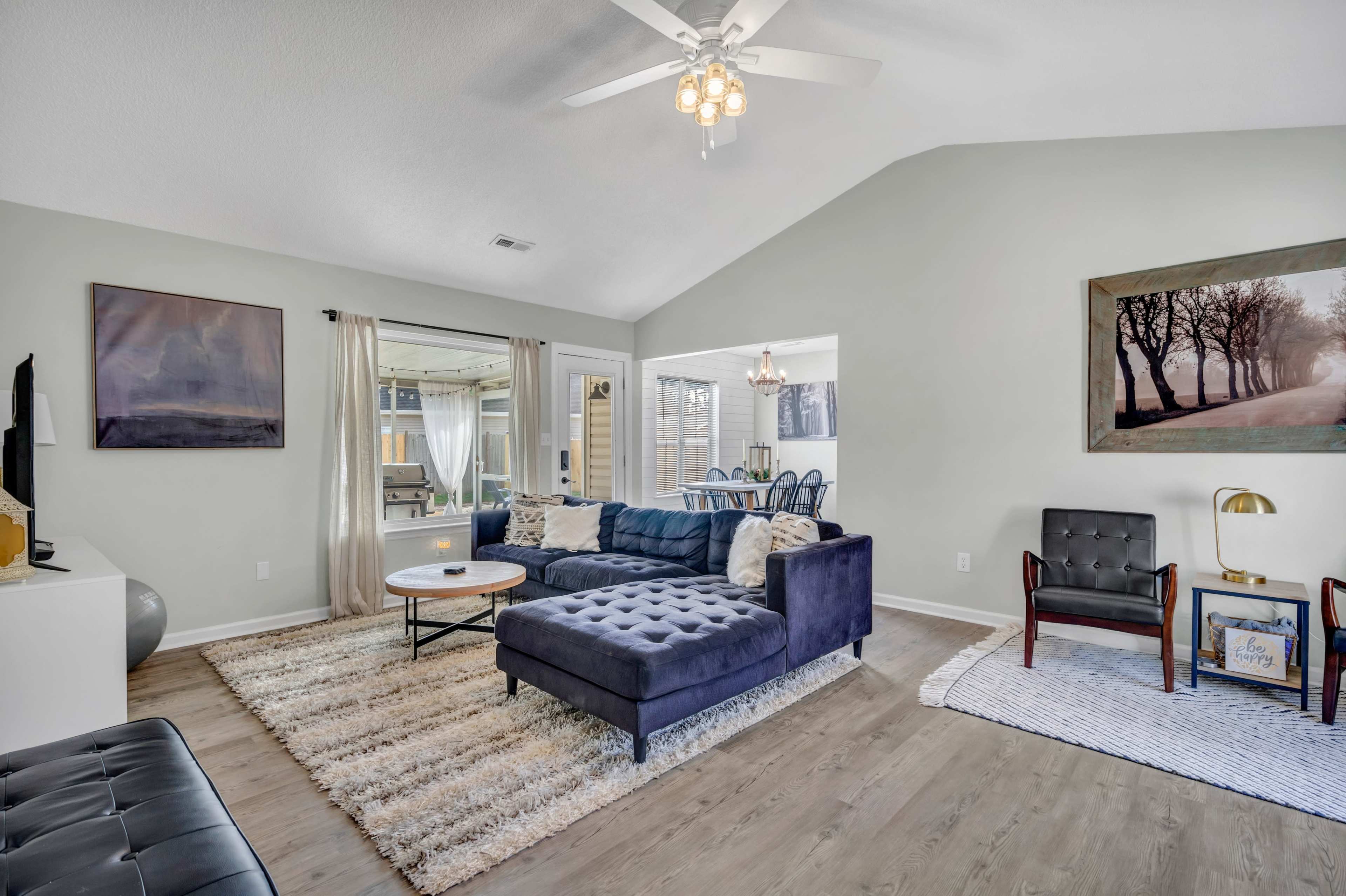 A spacious living room features a blue sectional sofa, a round coffee table, and large windows that provide natural light.