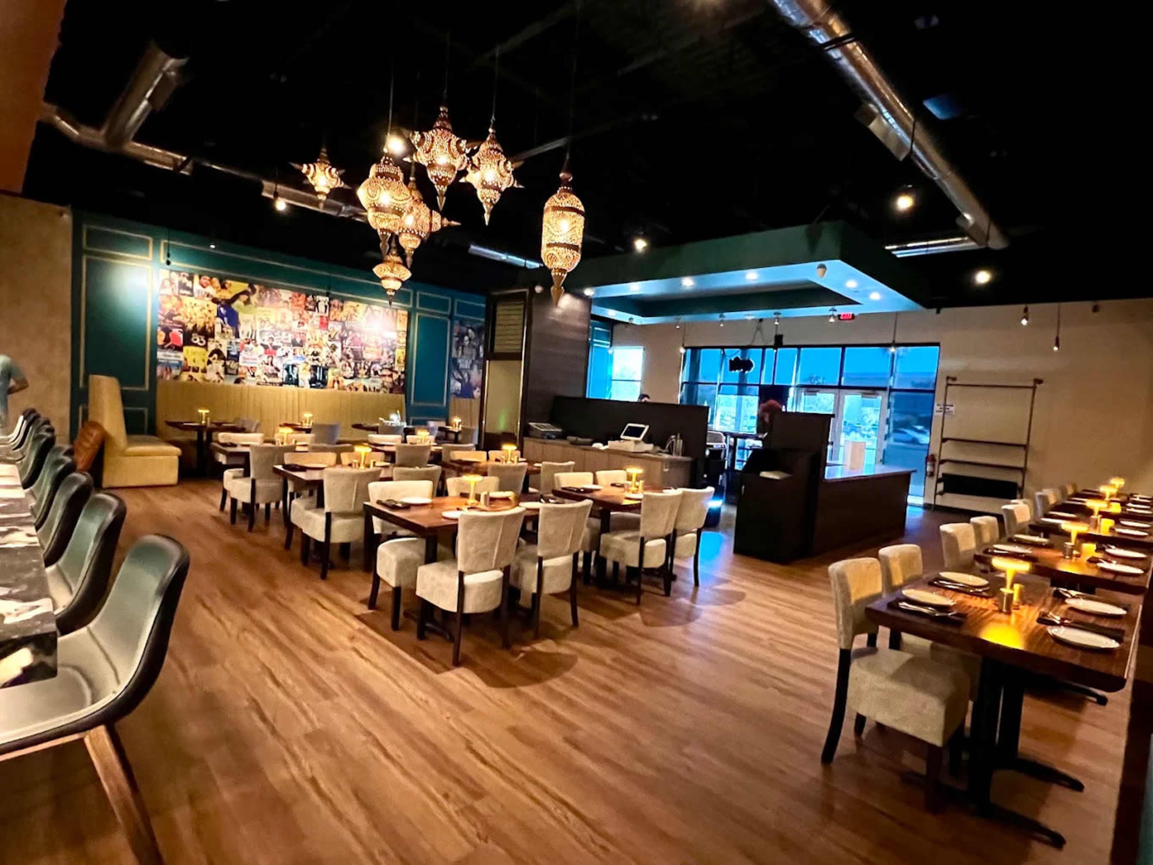 The image shows a spacious restaurant interior with wooden flooring, tables set for dining, and decorative light fixtures hanging from the ceiling.
