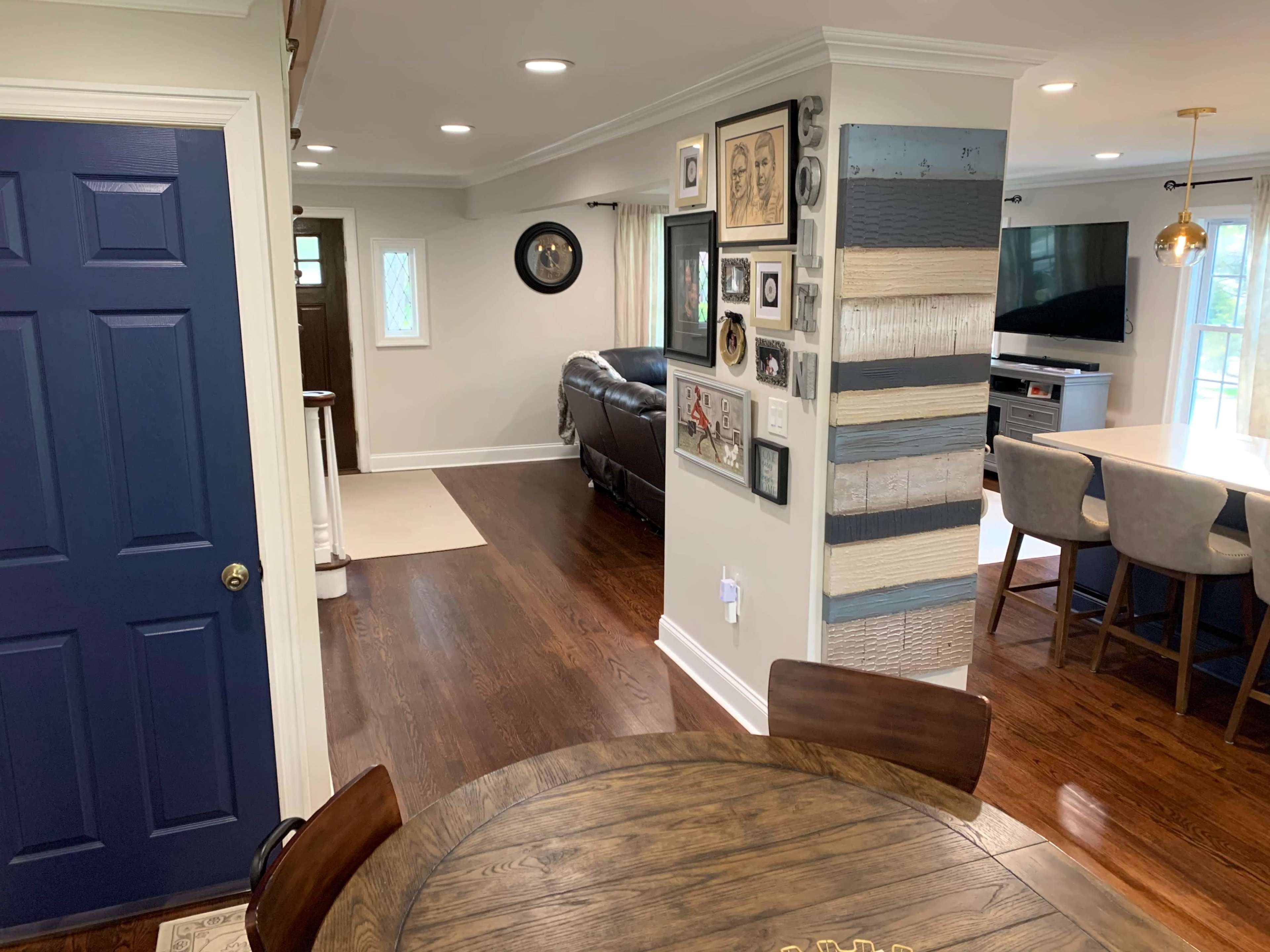 A modern interior space featuring a dining table, a blue door, and an adjoining living area with a leather sofa and wall decor.