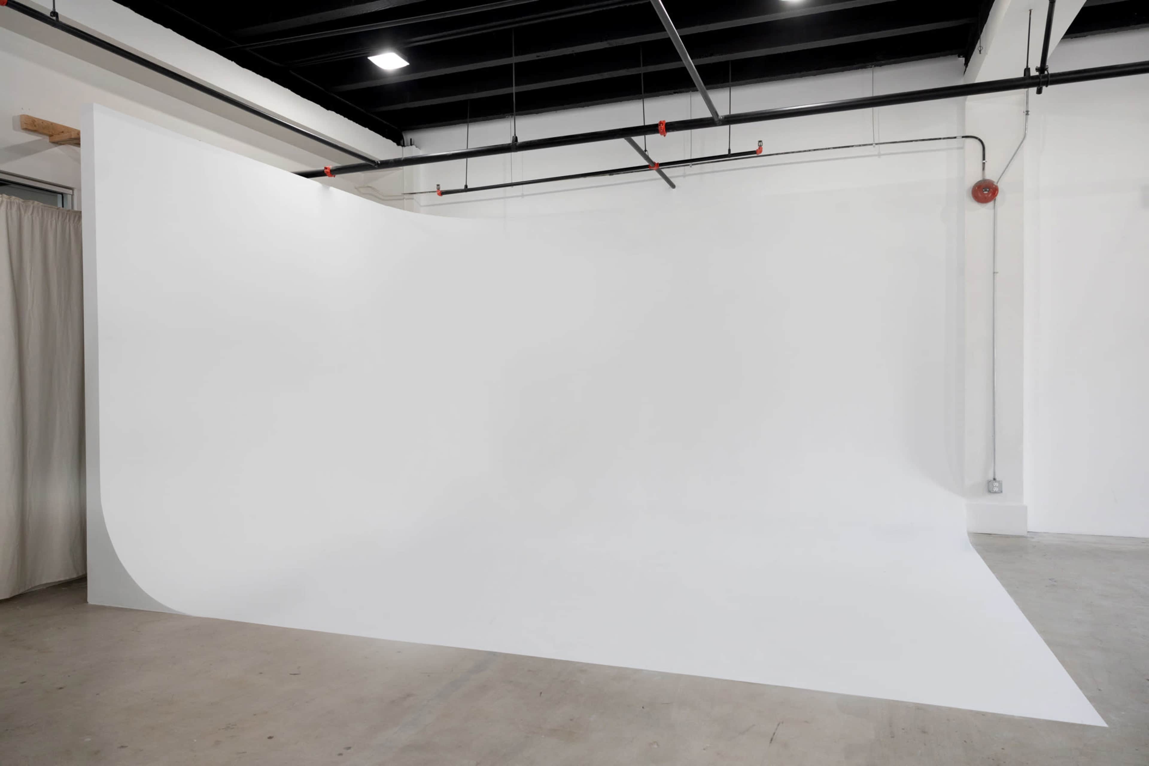 A spacious studio with a large, seamless white backdrop and concrete flooring.