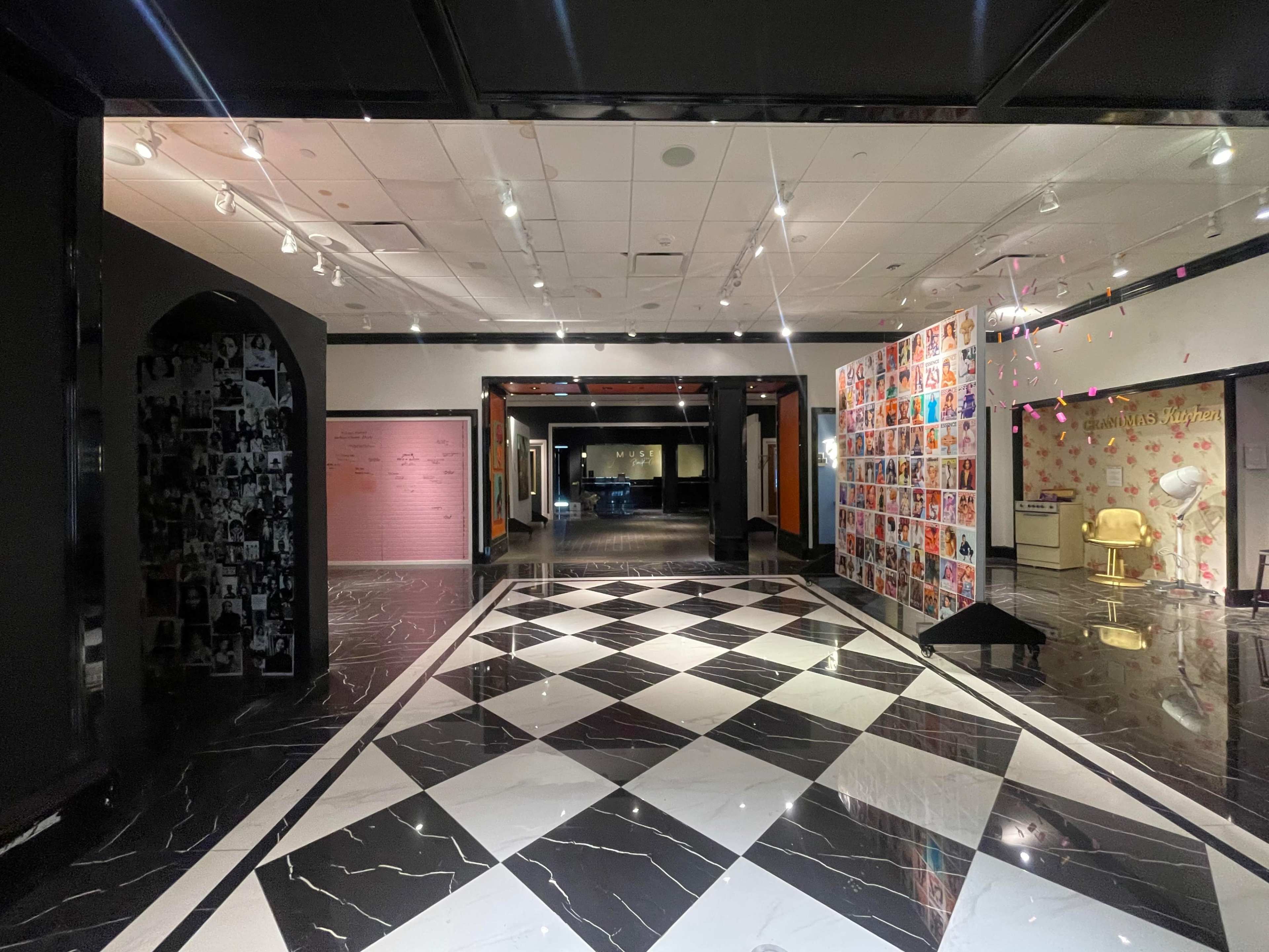 A spacious gallery with a checkered black and white floor, featuring walls adorned with colorful photographs and text.